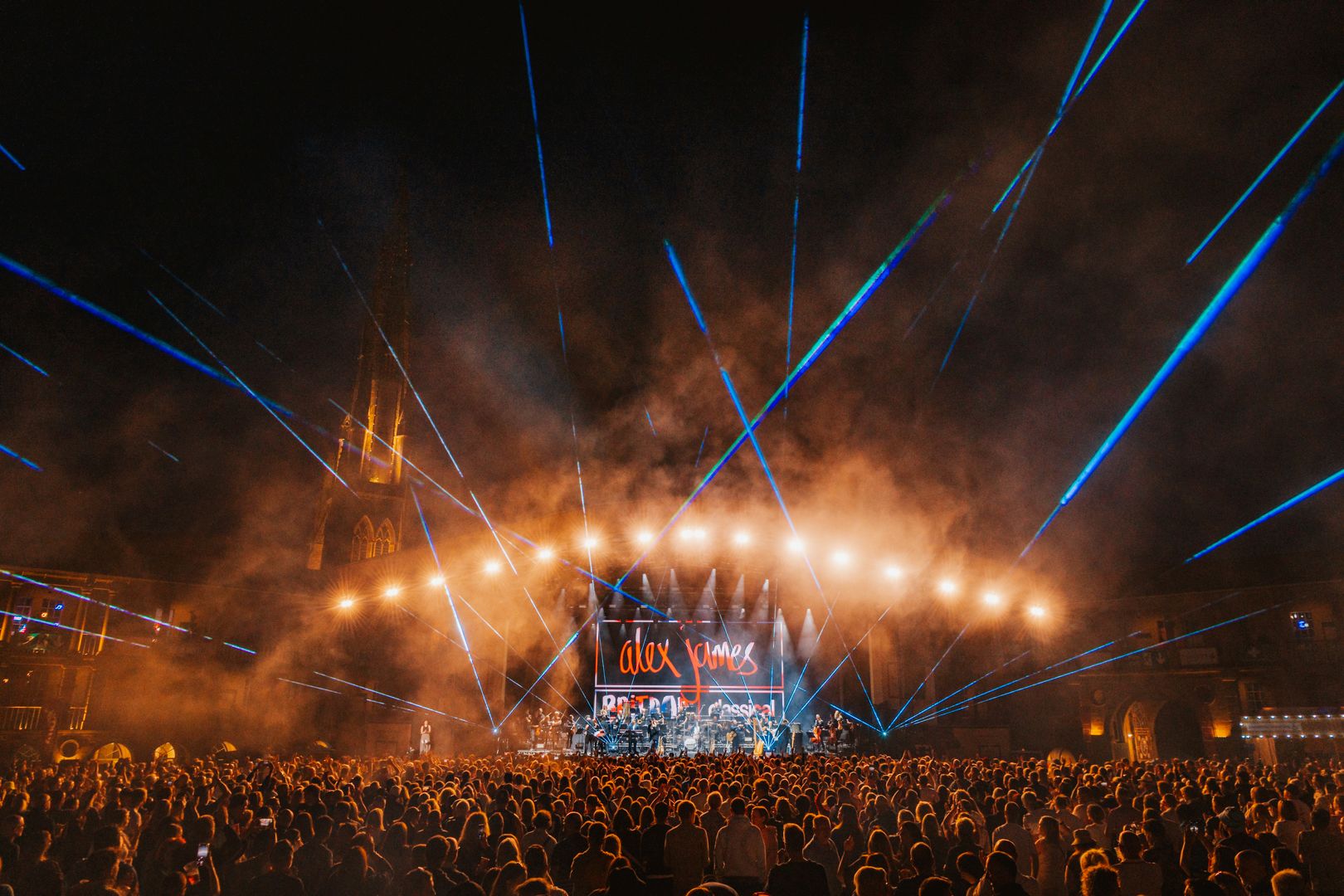 Nighttime outdoor concert with blue lasers and large crowd
