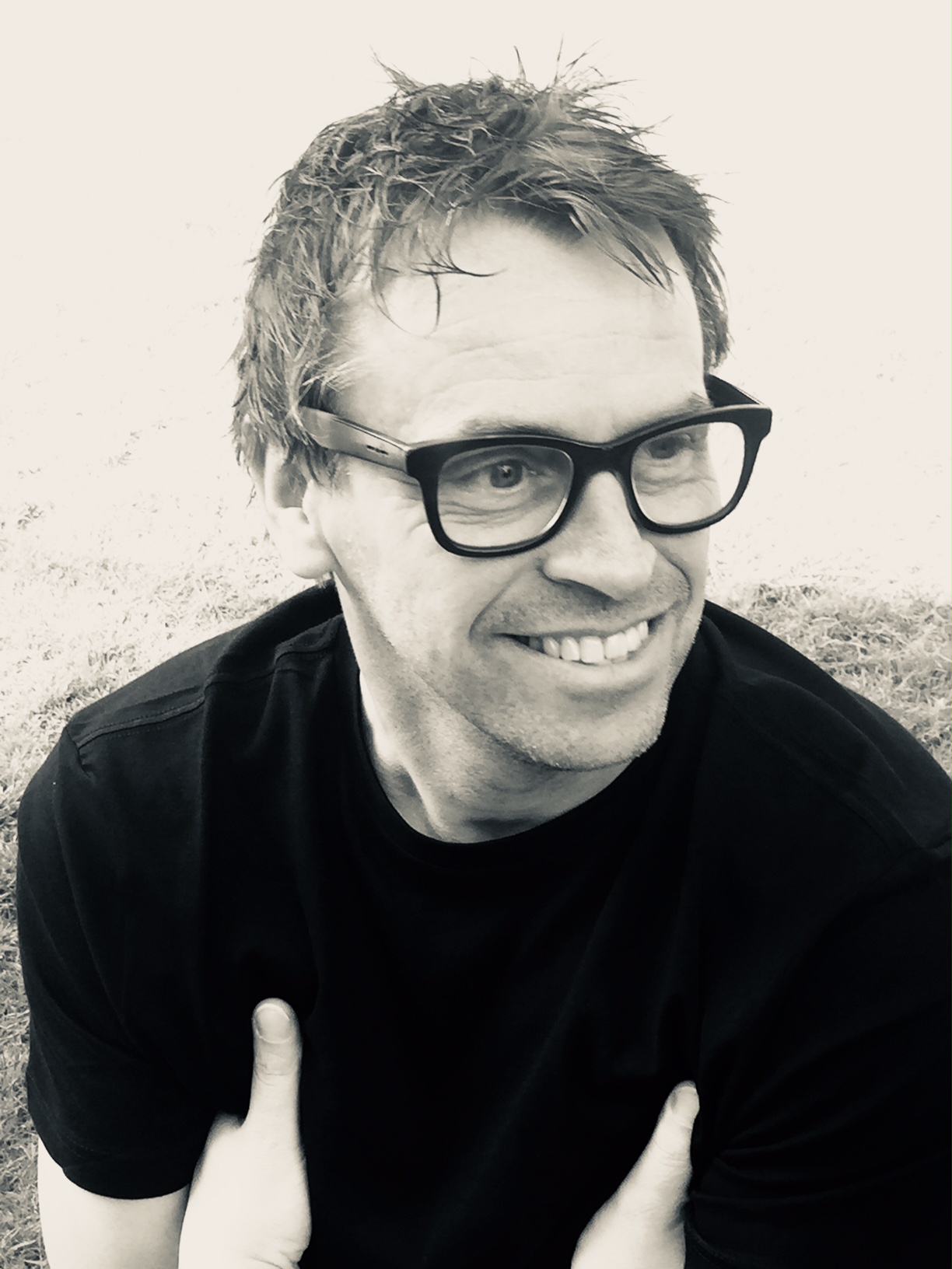Smiling person with glasses in a grassy outdoor setting