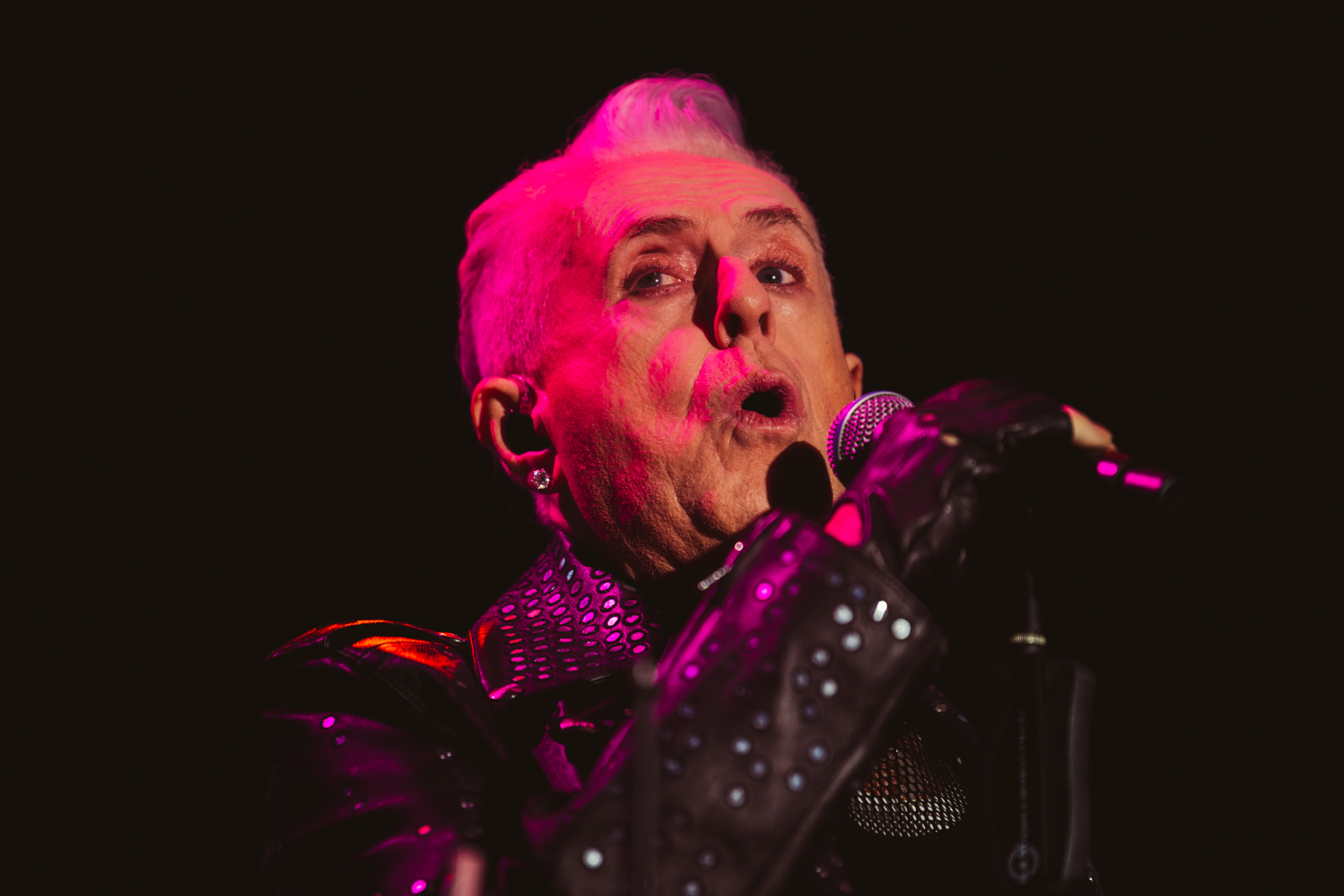 Elderly singer in studded leather jacket performing on stage