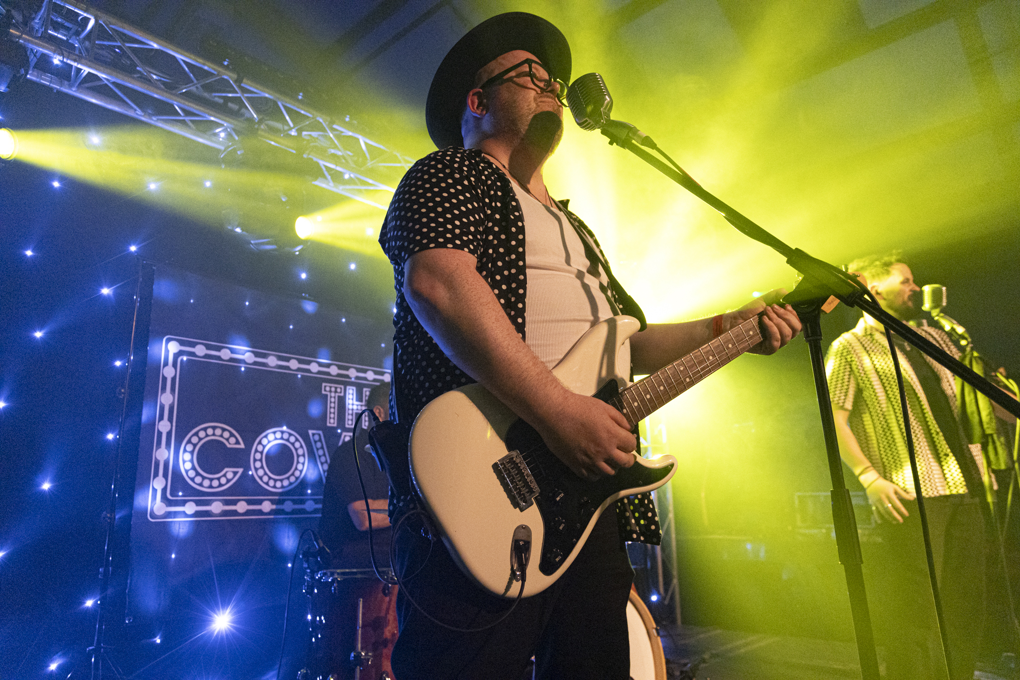 Musician in hat playing electric guitar under bright stage lights