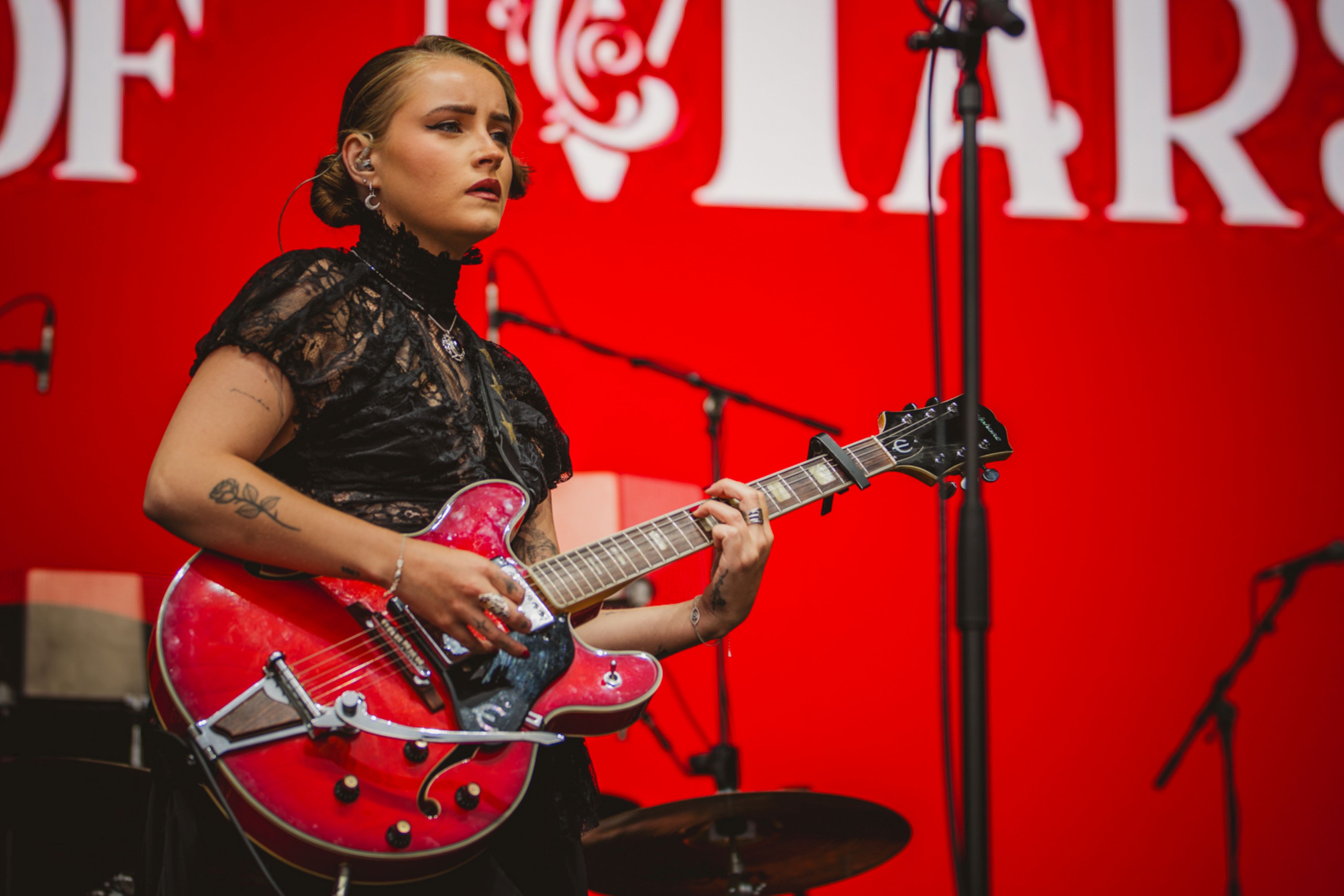Female guitarist in black lace dress playing red guitar on stage
