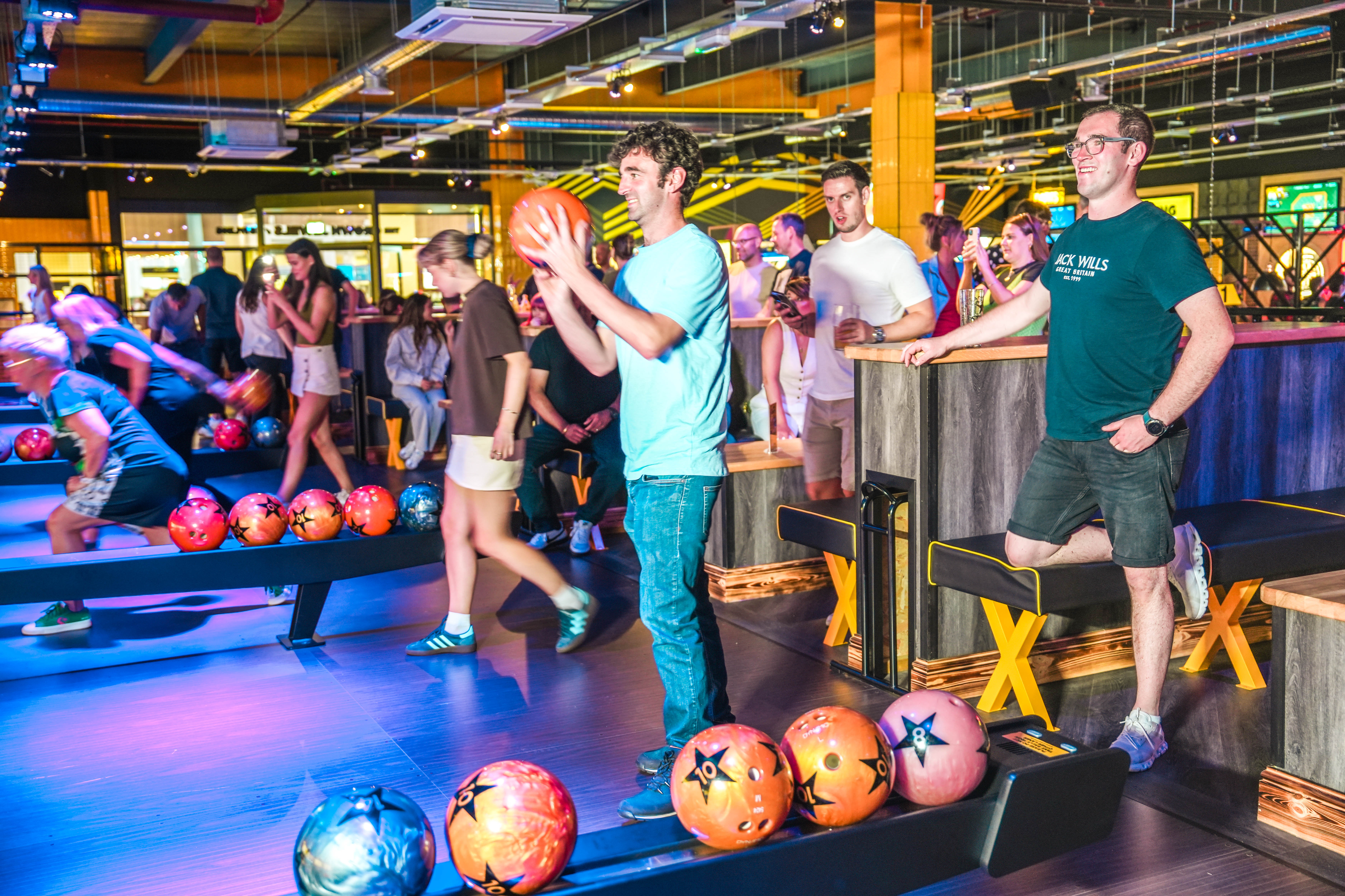 People bowling in a lively, colourful indoor alley with neon lights