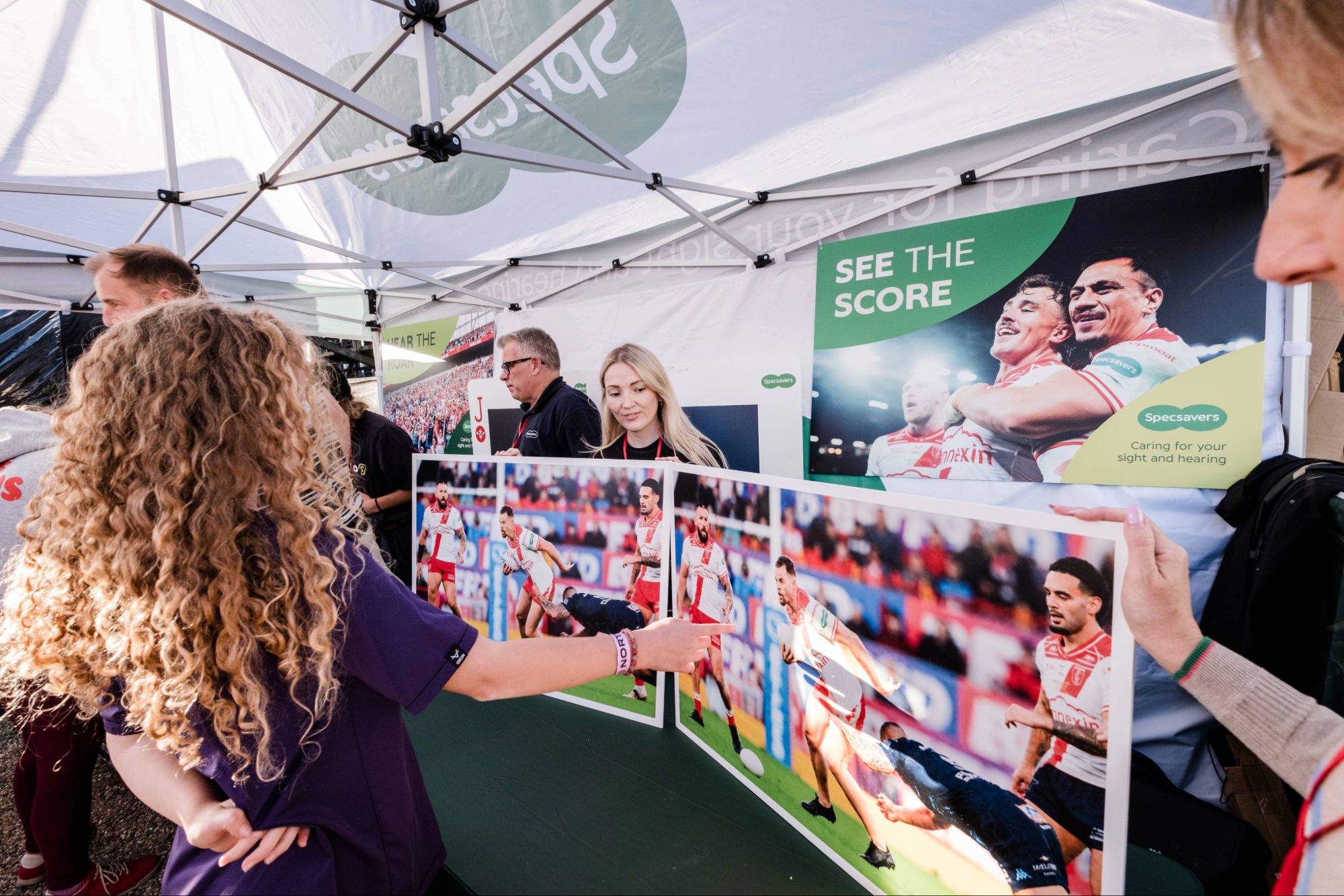 People at an outdoor sports event booth with rugby posters