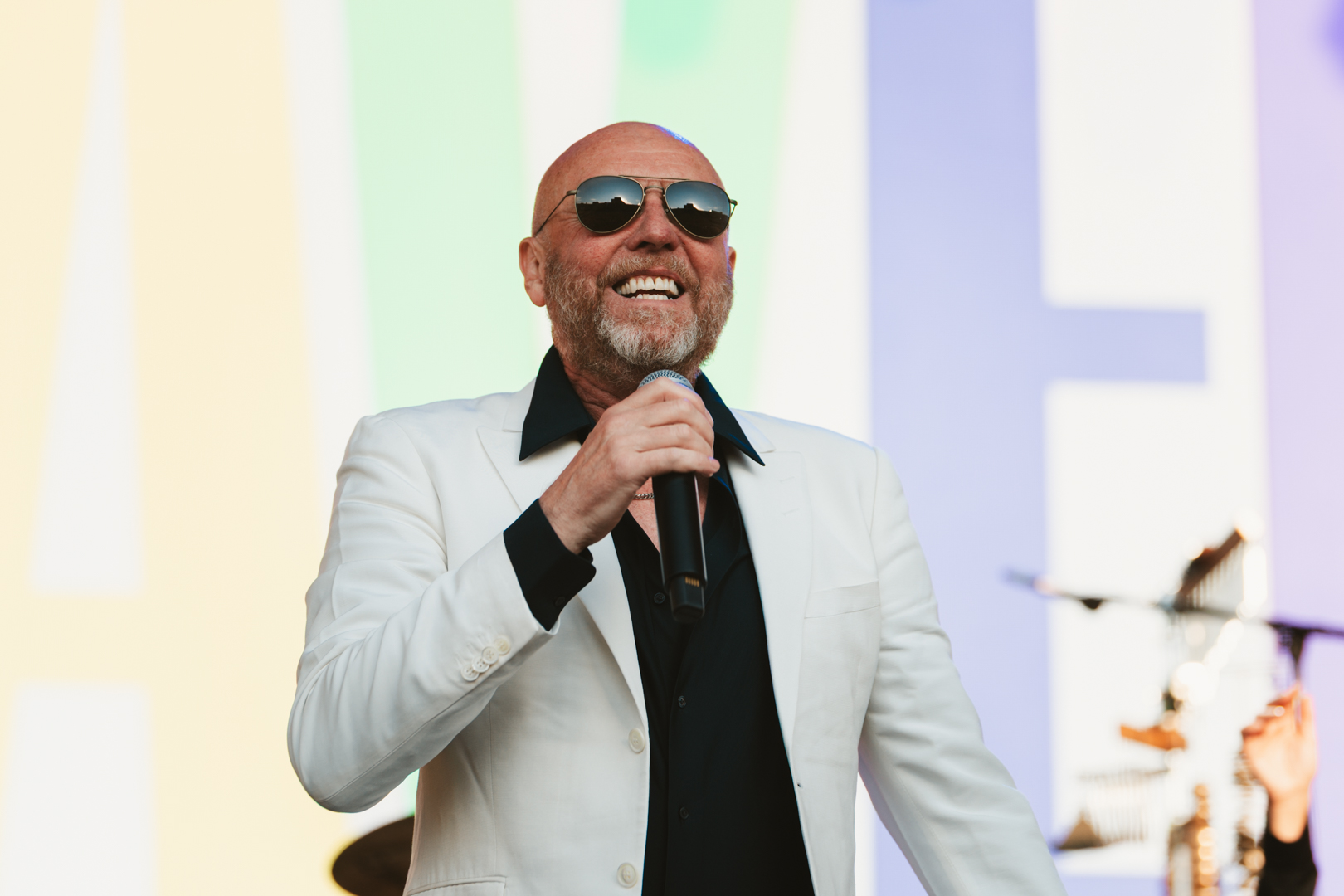 Smiling man in white blazer and sunglasses holding a microphone