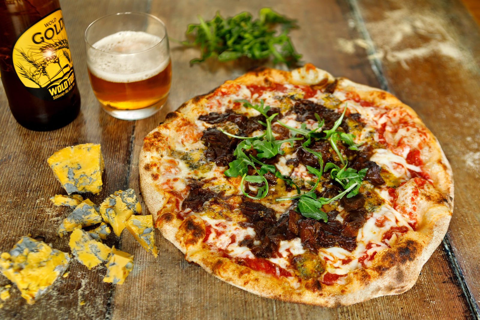 Wood-fired pizza with cheese and arugula, beer bottle nearby