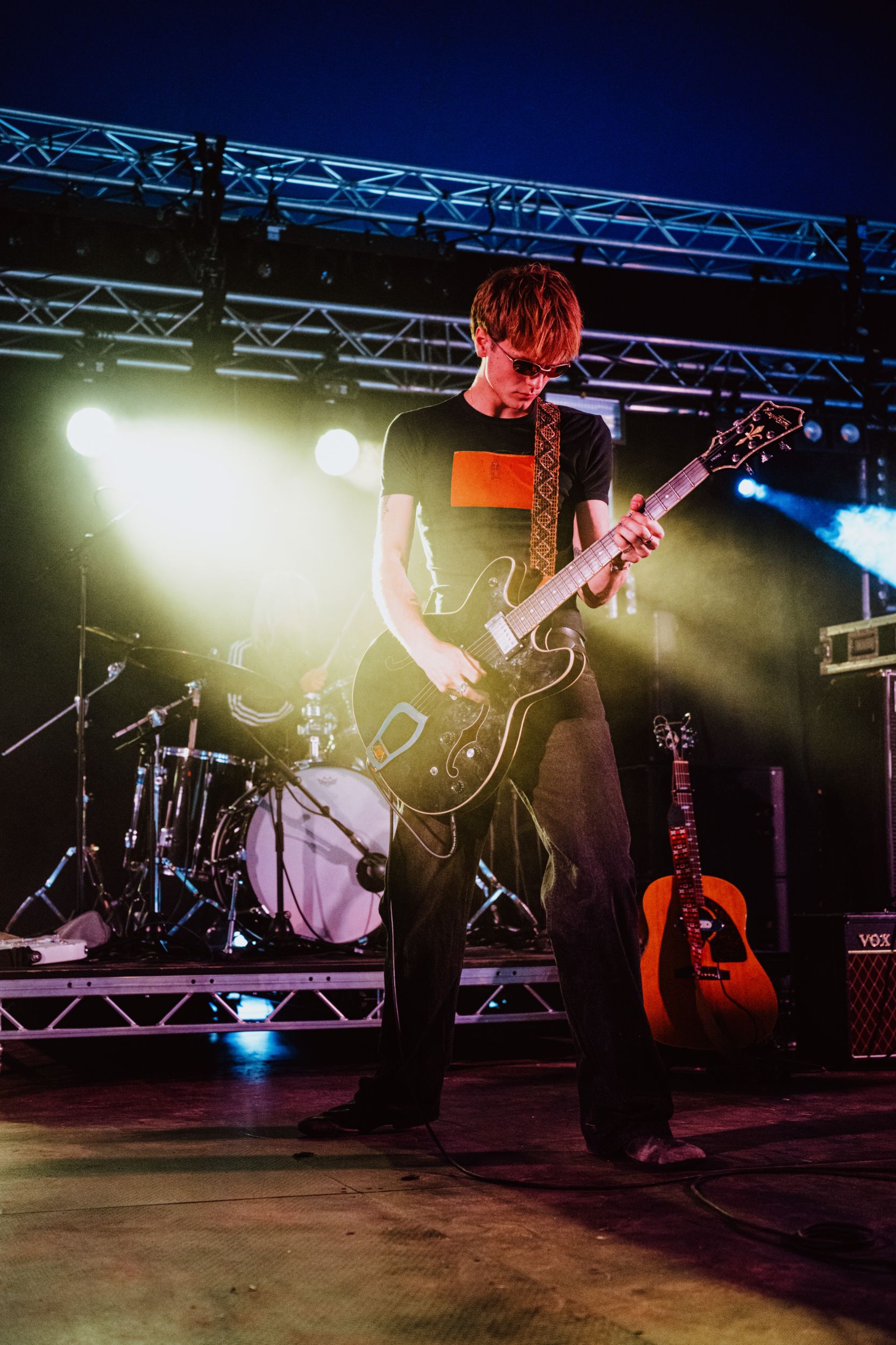 Guitarist performing energetically on stage with bright lights