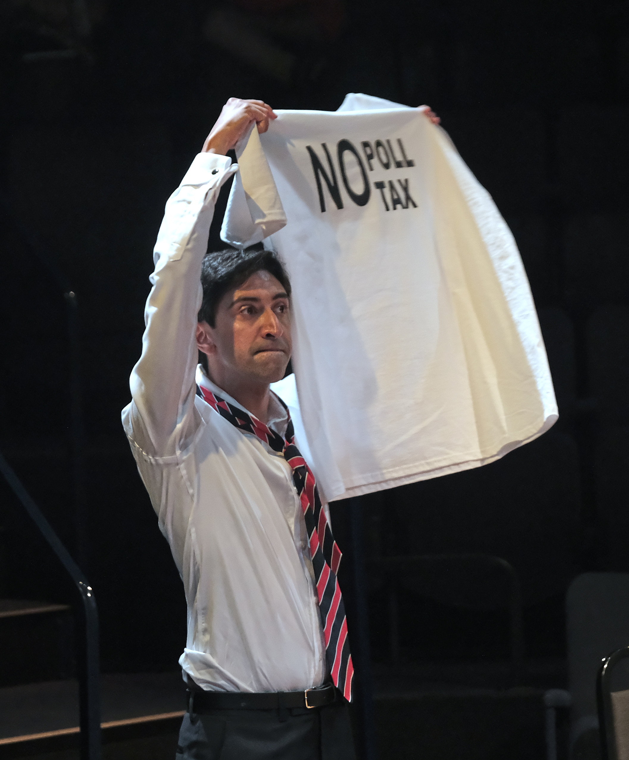 Man in white shirt holding a 'No Poll Tax' T-shirt on stage