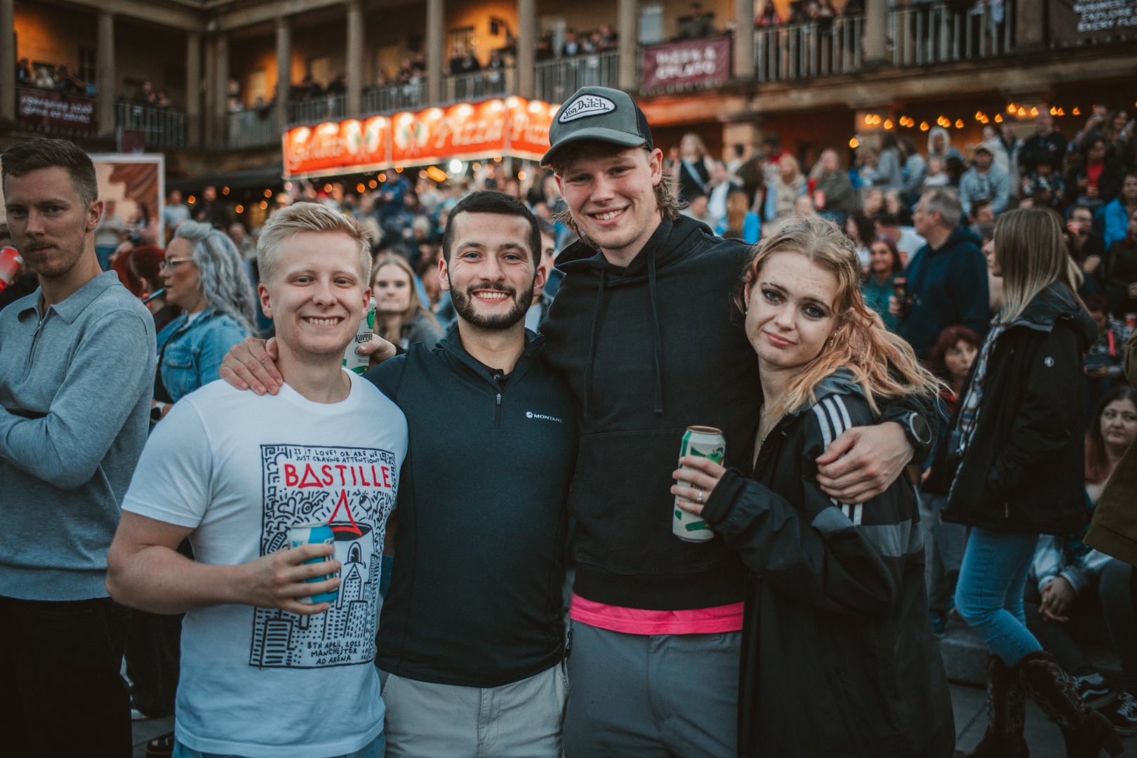 Group of friends smiling at an outdoor festival with lively crowd