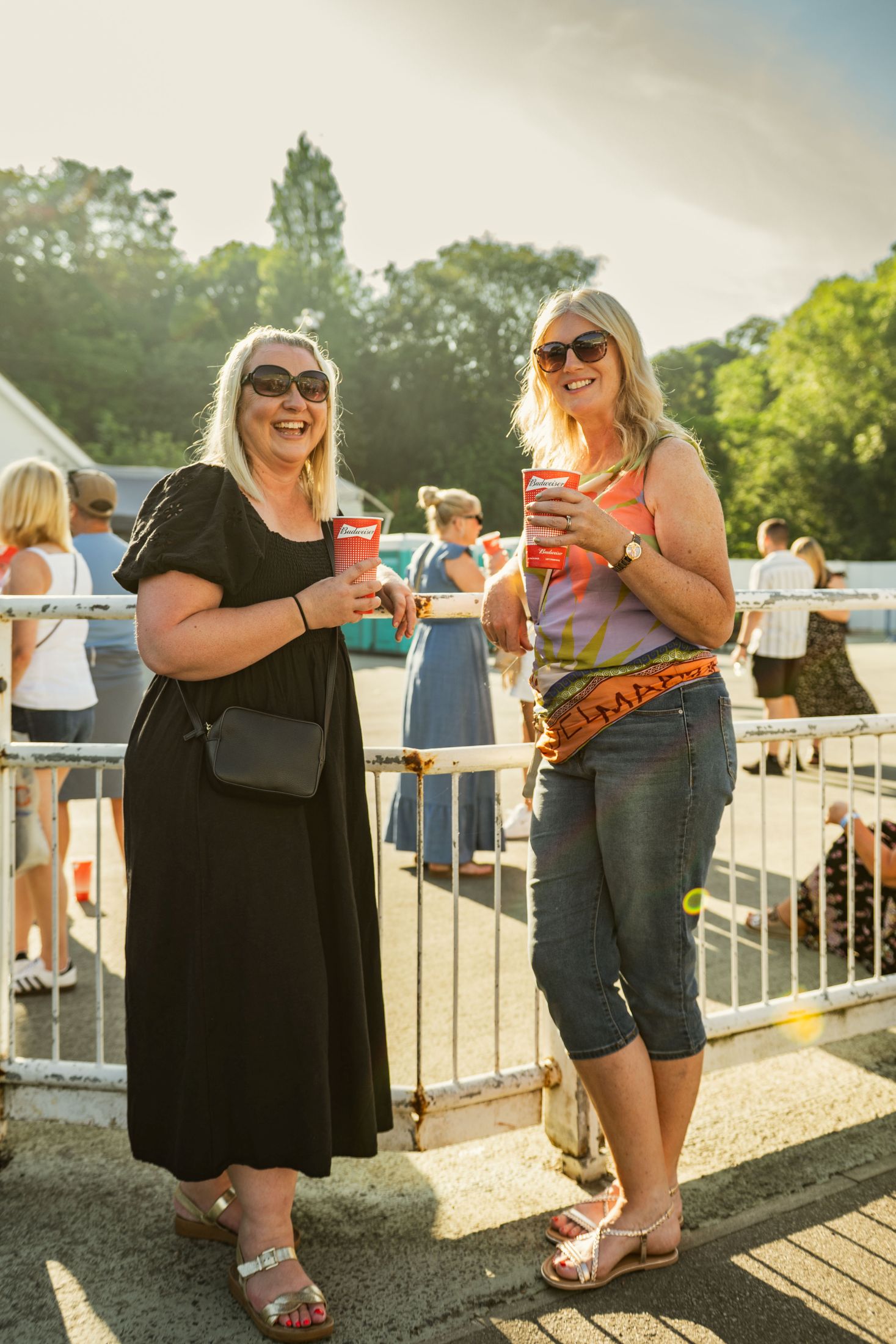 Two women enjoying drinks at an outdoor event in sunshine