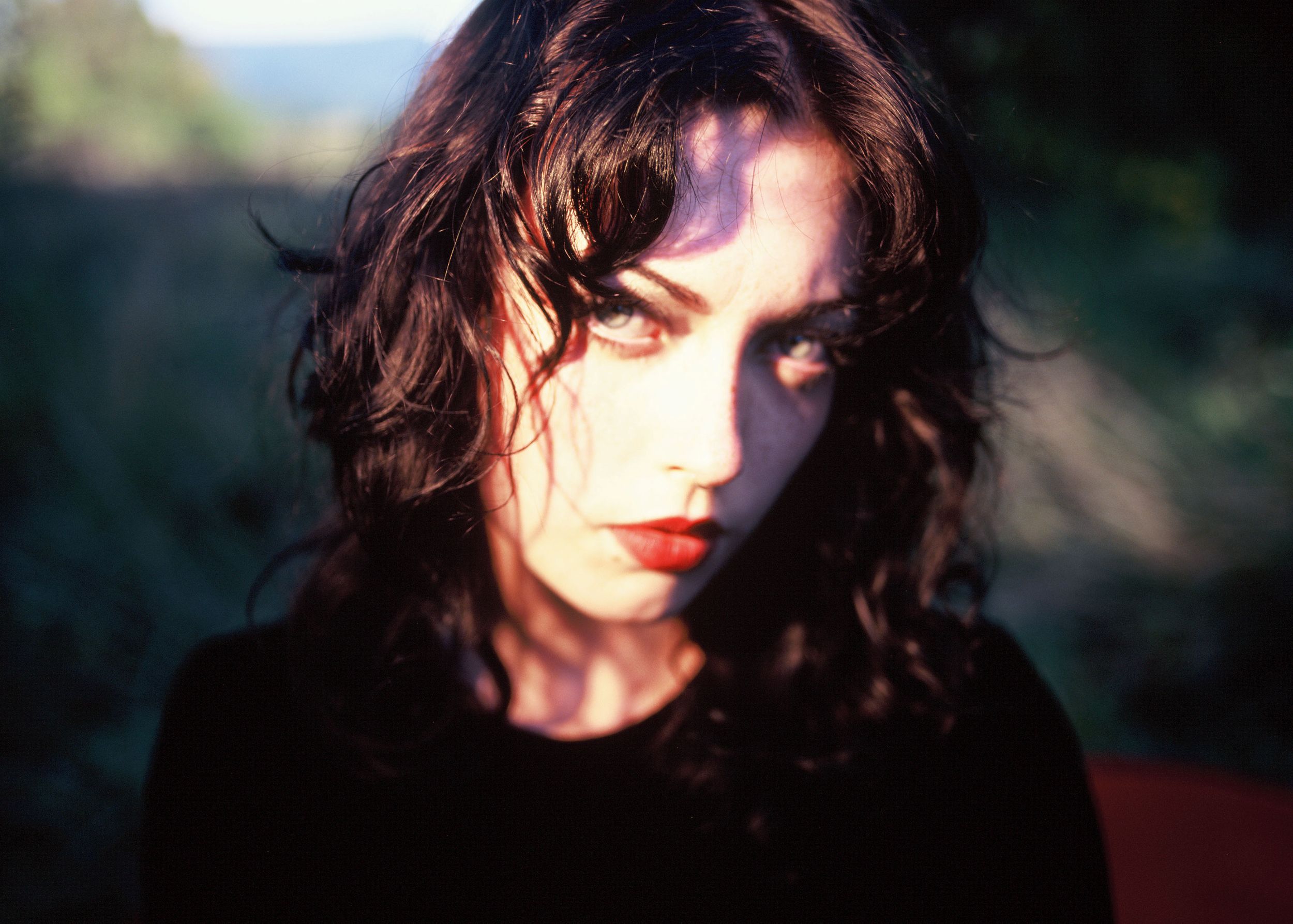 Woman with dark curly hair in shadowy outdoor setting