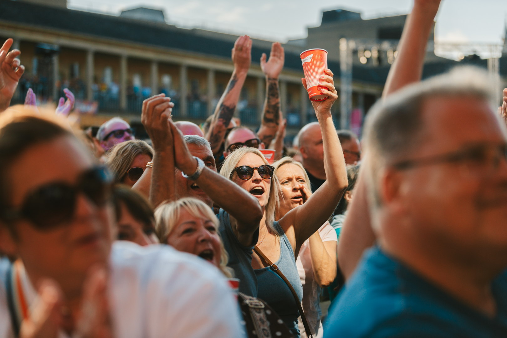 Crowd enjoying a summer festival, people cheering with drinks
