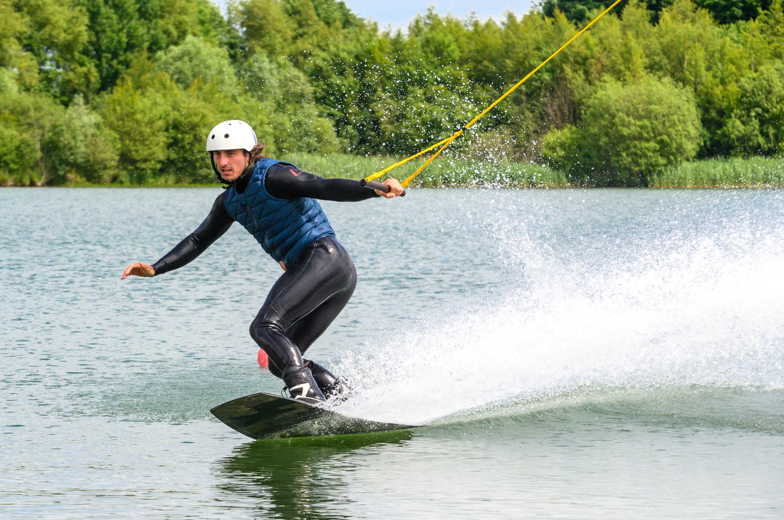 Man wakeboarding on lake with lush green trees in background