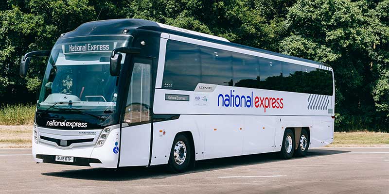 White National Express coach bus on road with trees behind