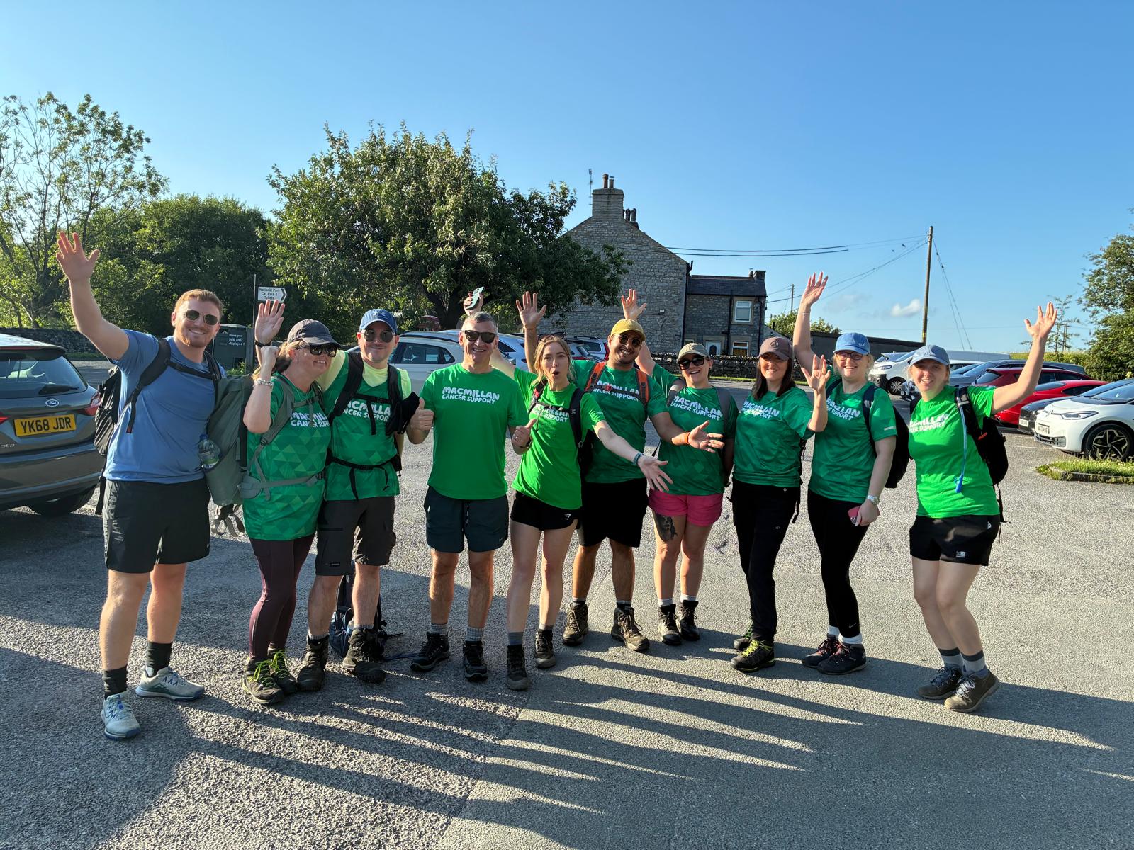 Group of hikers in green shirts waving outside stone cottage