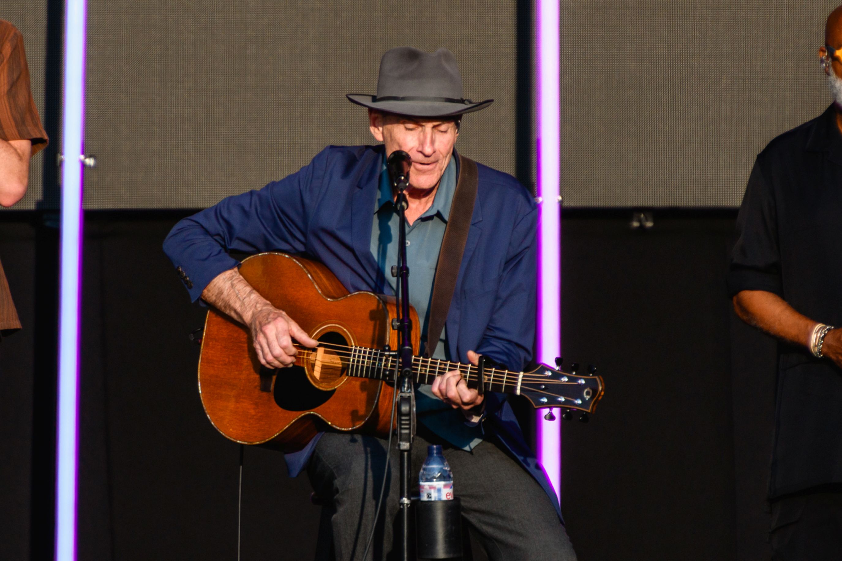 Musician playing acoustic guitar on stage wearing a grey hat