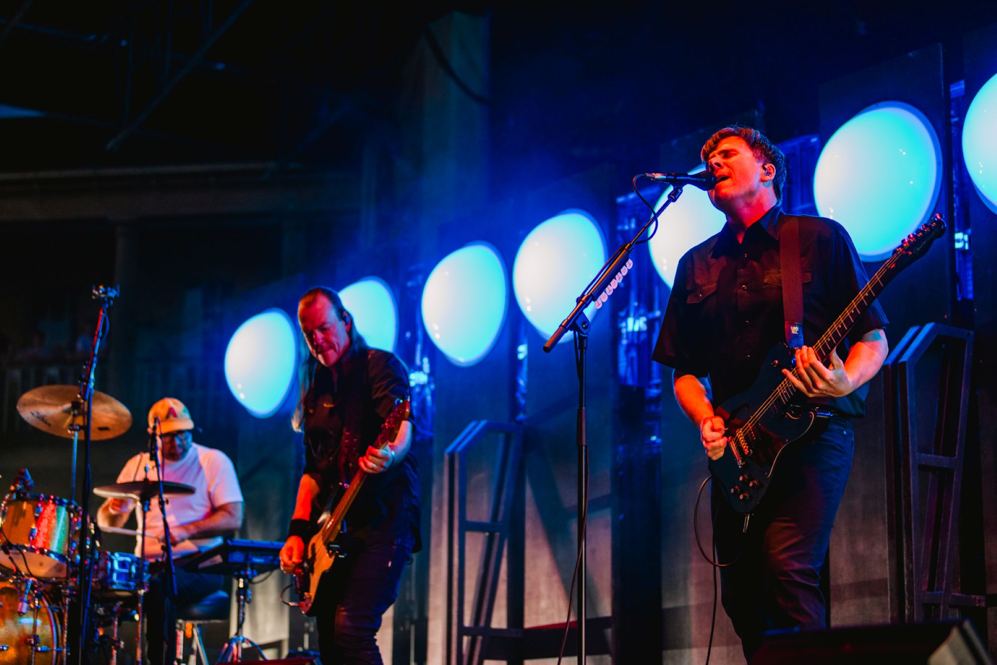 Three musicians performing on stage with blue lights