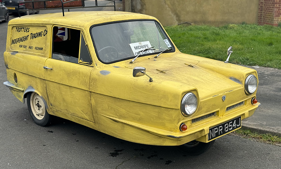 Yellow three-wheeled car with sign parked on roadside