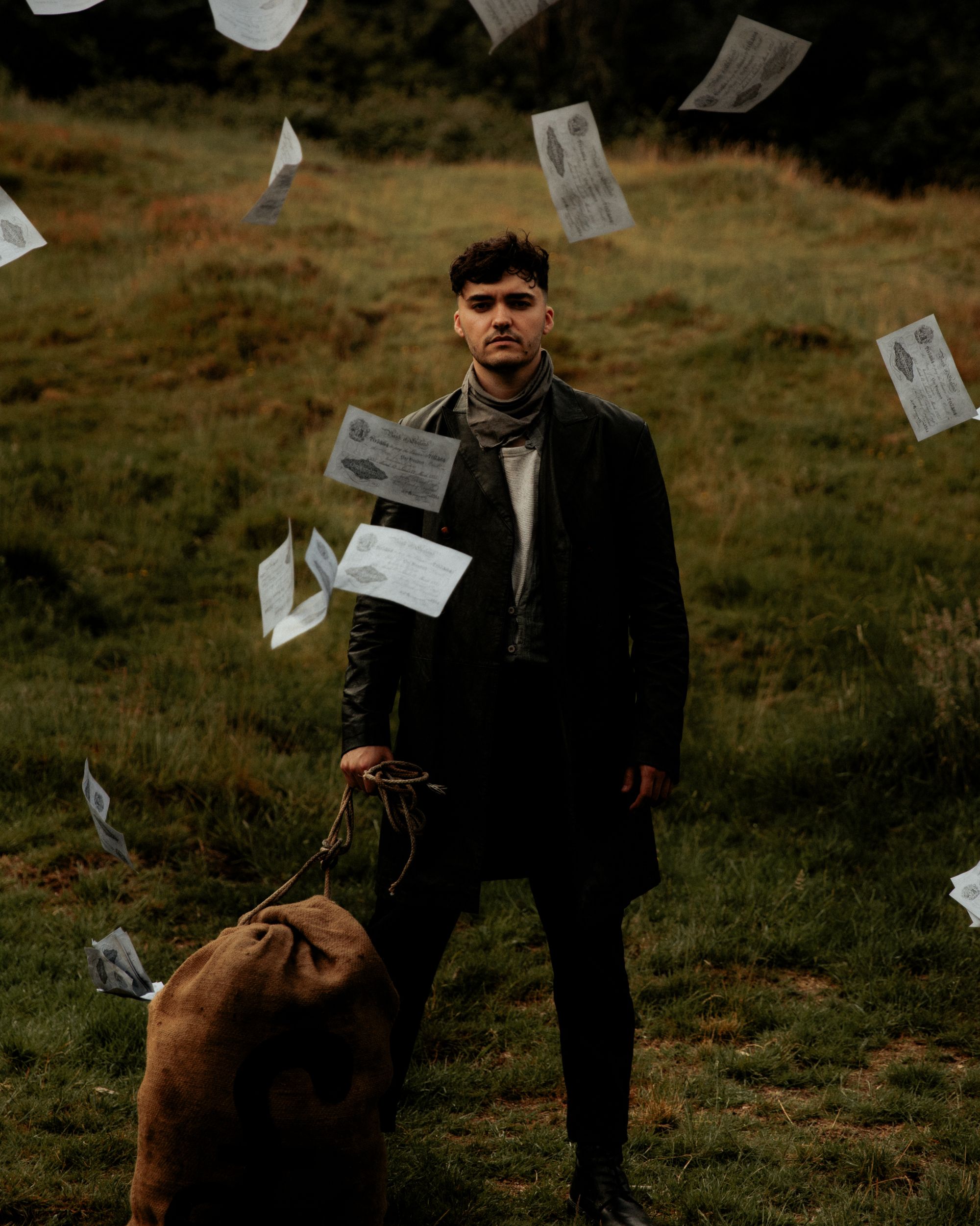 Man standing in field with flying letters and large sack