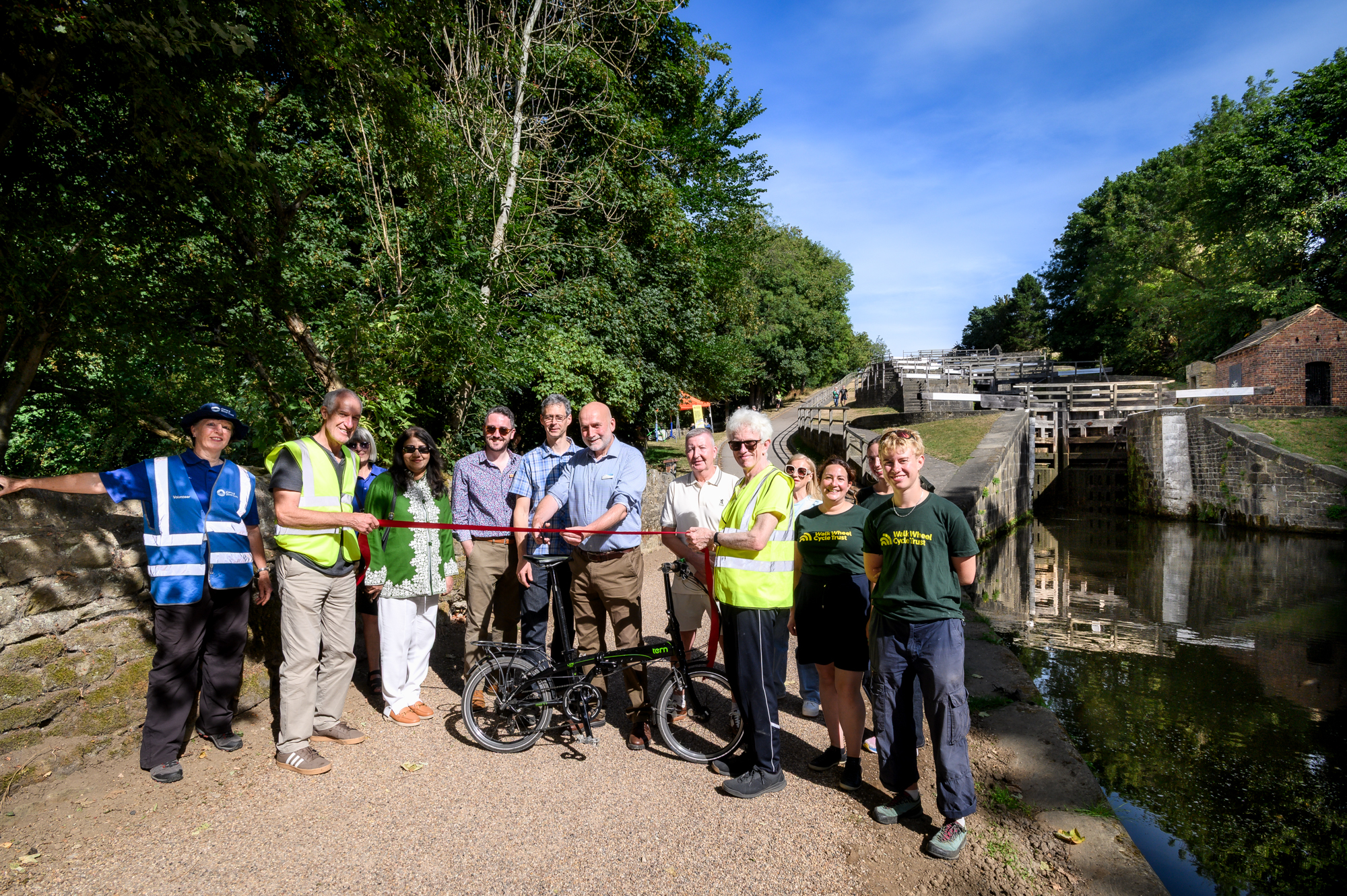 Group of people cutting ribbon at Bingley Five Rise Locks surrounded by trees