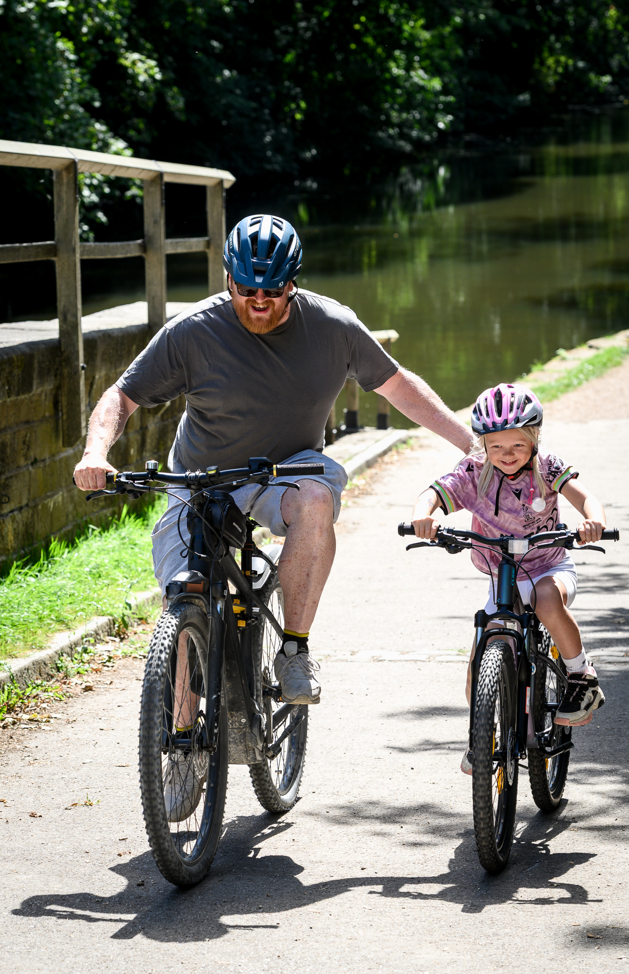 Father and daughter cycling along a canal path in summer