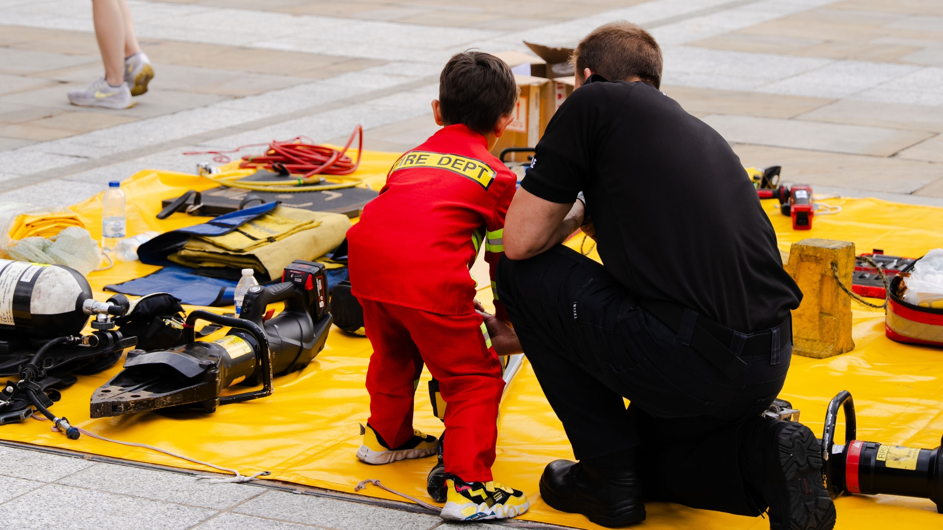 Child in red fire department suit with firefighter on plaza