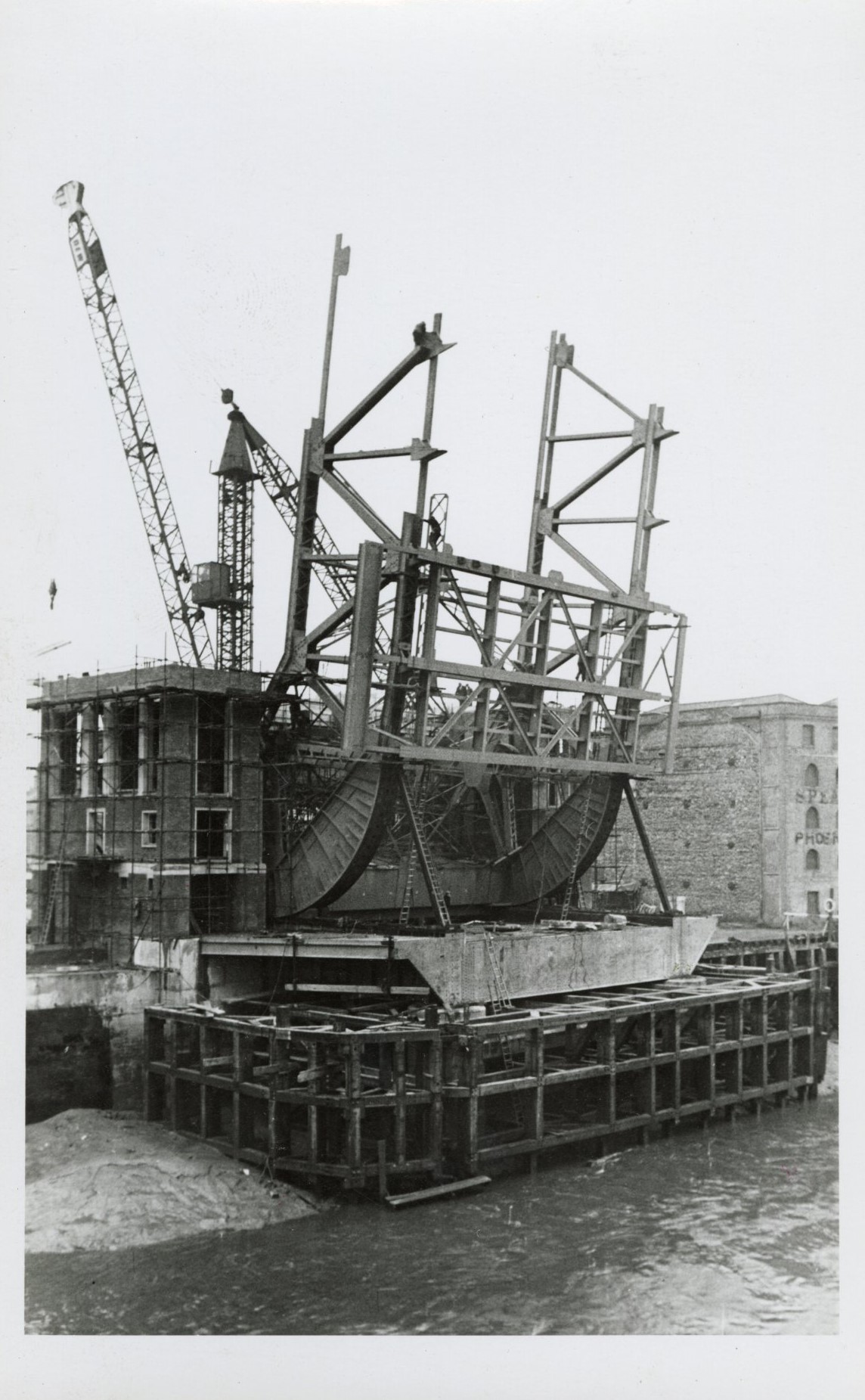 Historic bridge under construction over river with cranes