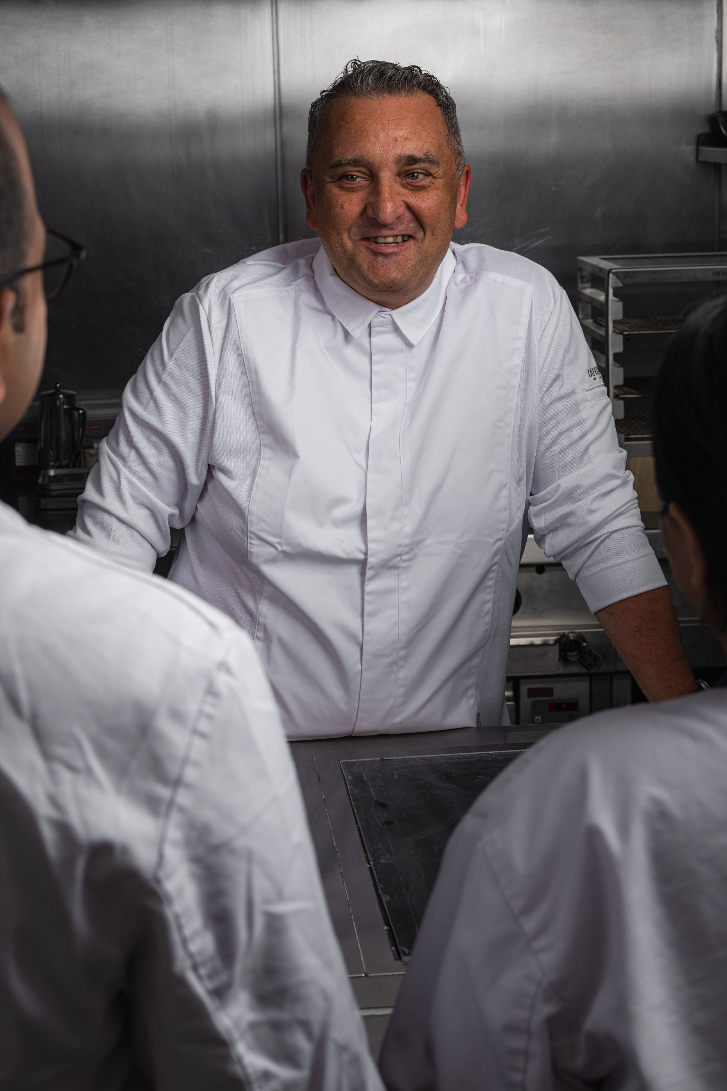 Chef in white uniform smiling while talking to staff in kitchen