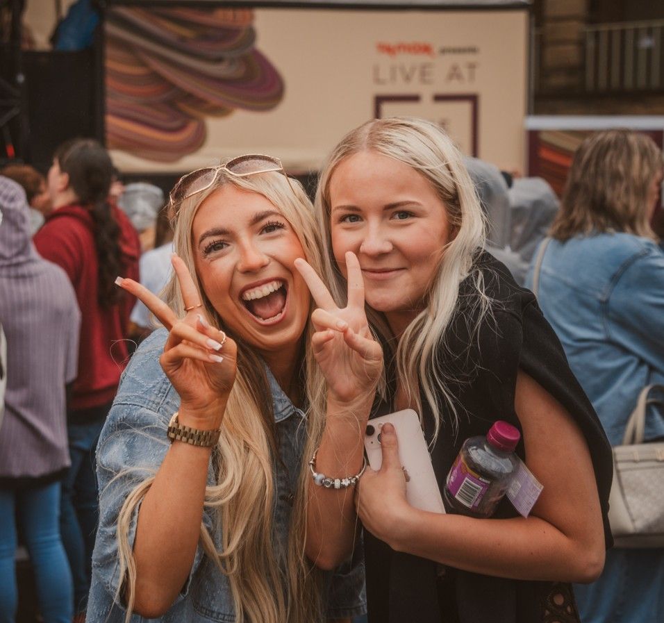 Two smiling young women giving peace signs at outdoor event