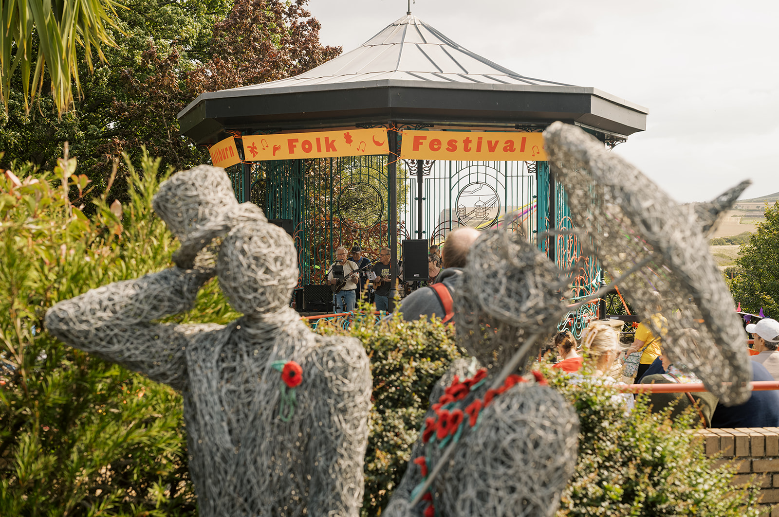 Wire sculptures of people in hats near bandstand at folk festival