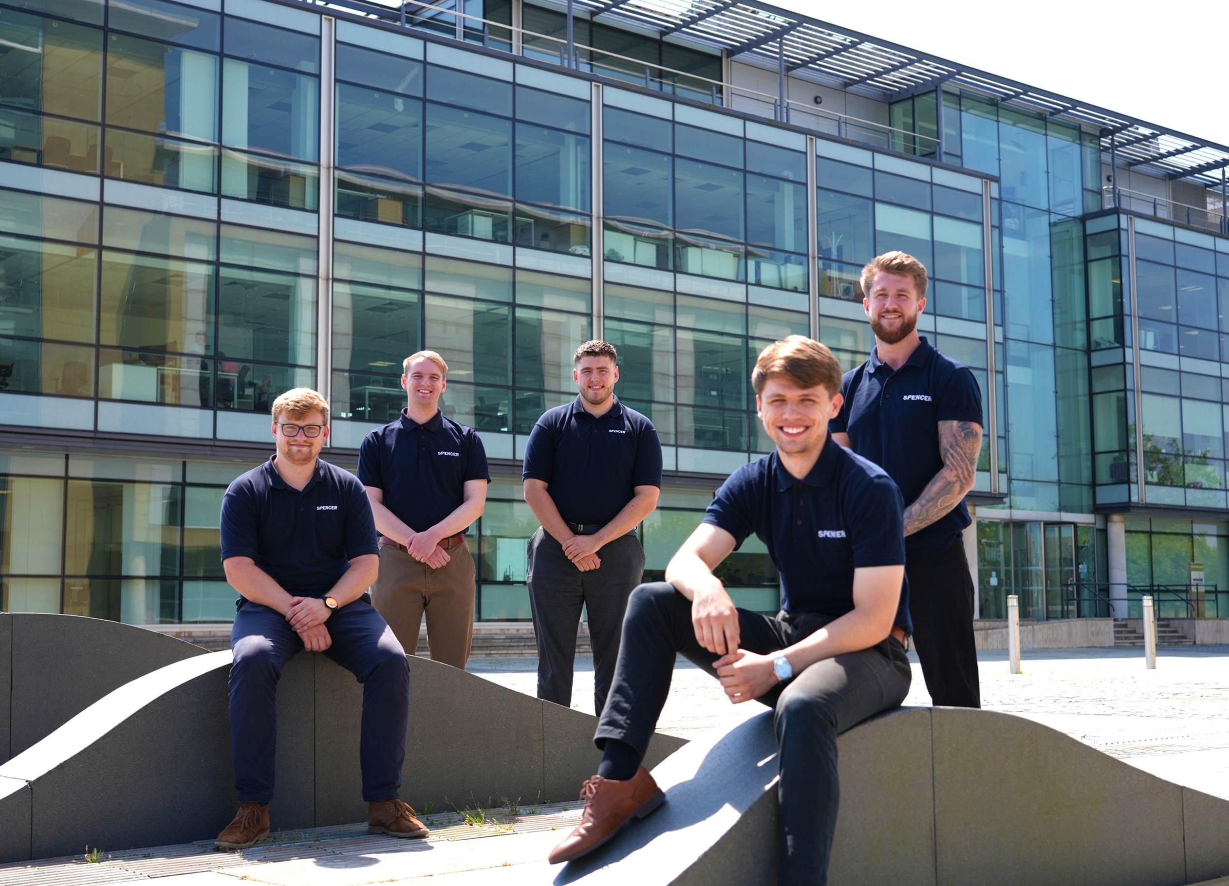 Group of five men in matching navy shirts outside modern glass building