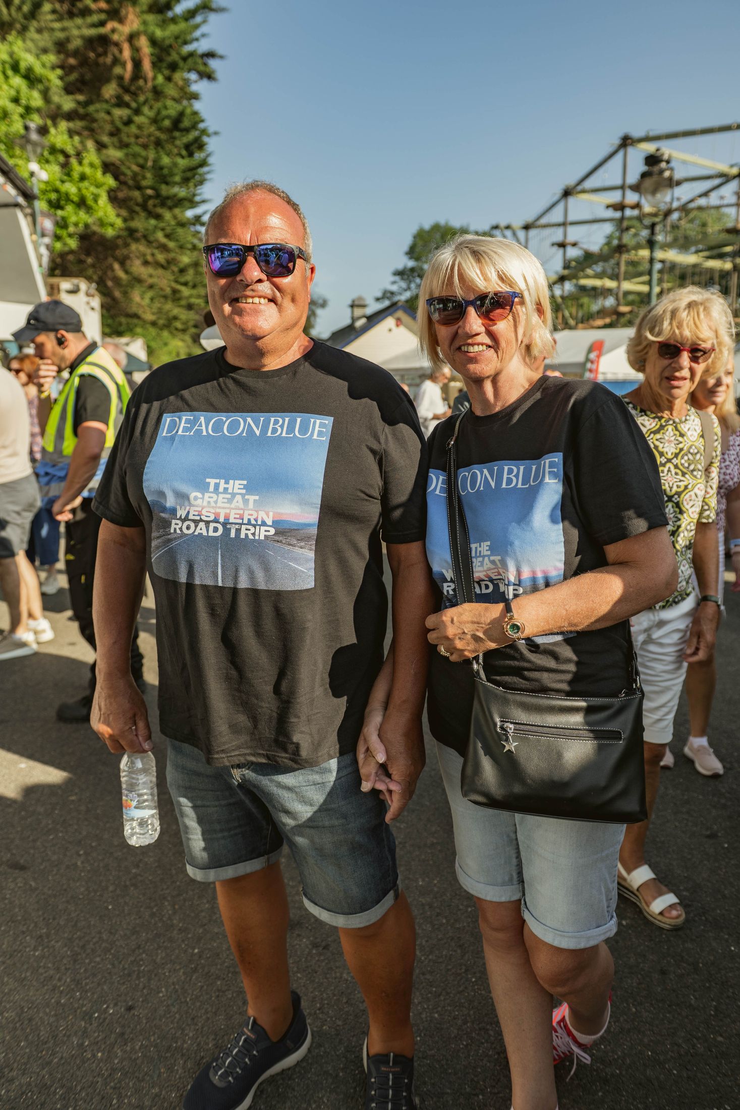 Couple in matching band t-shirts holding hands at outdoor event