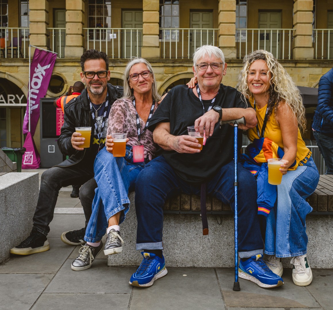 Group of four smiling adults sitting with drinks in town square