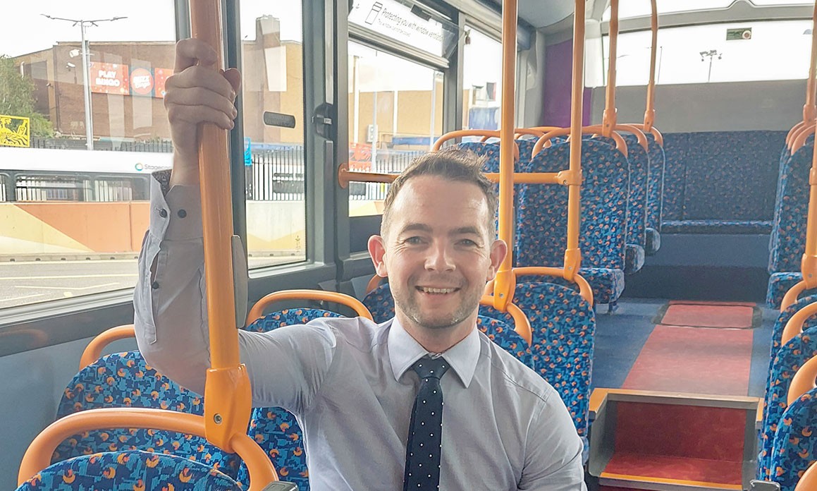 Smiling man in a tie on an empty double-decker bus with blue seats