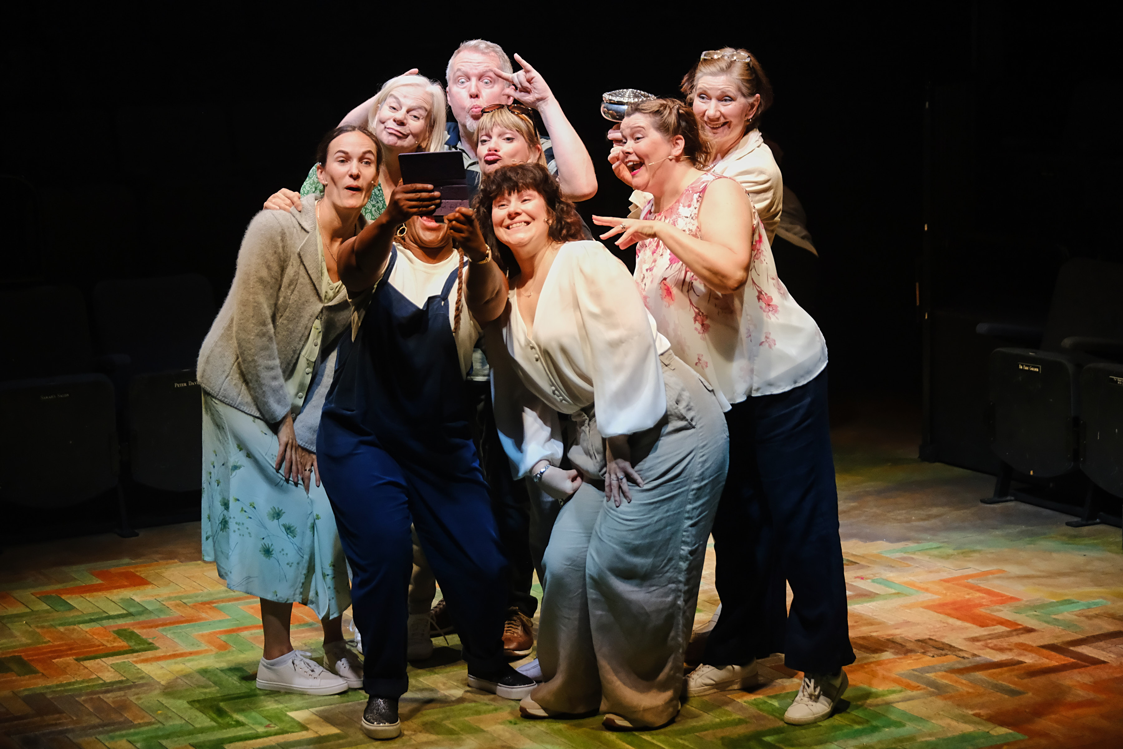 Group of seven people posing for a selfie on a theatre stage