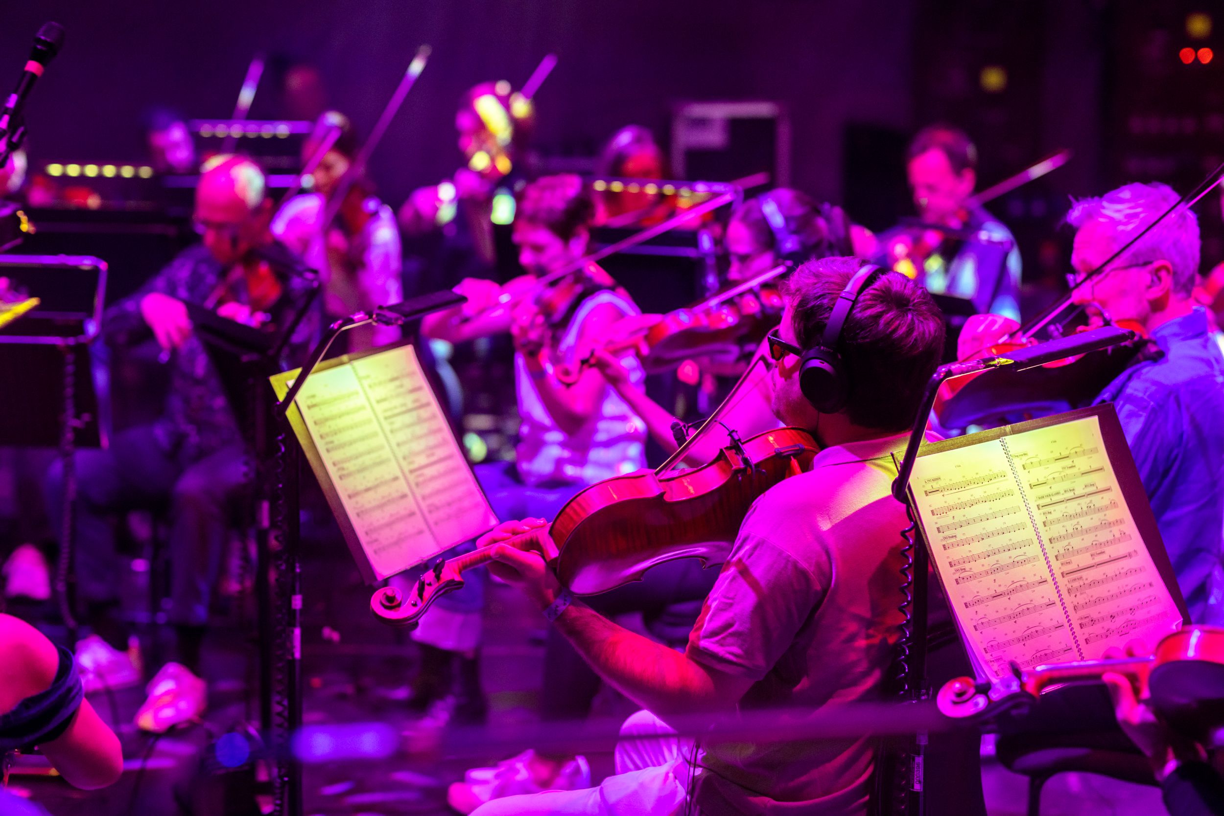 Orchestra performing under purple lights with sheet music