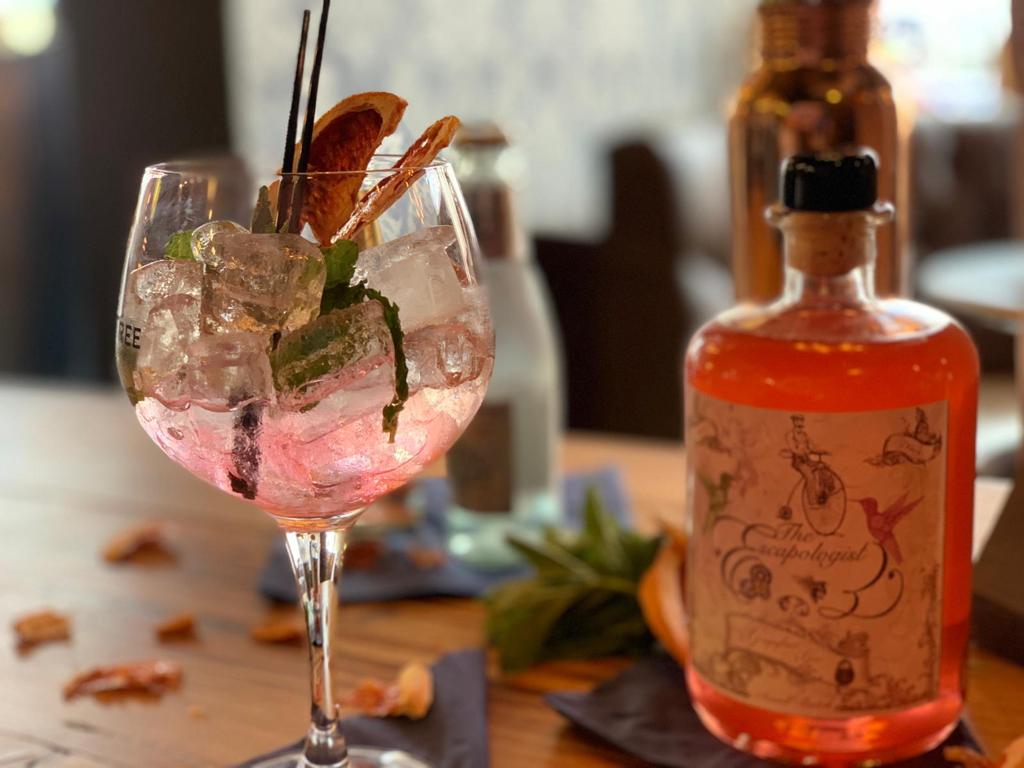 Pink gin cocktail with garnish and bottle in cosy bar
