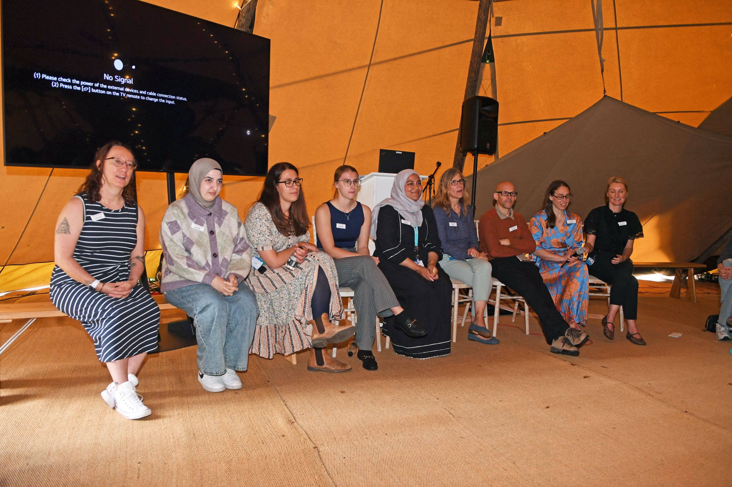Panel of diverse speakers seated in a large, tented space