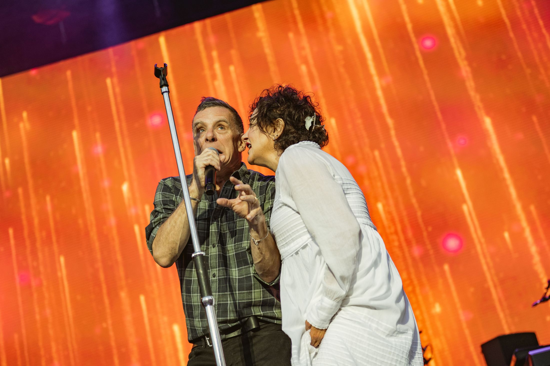 Man and woman singing on stage with vibrant orange backdrop