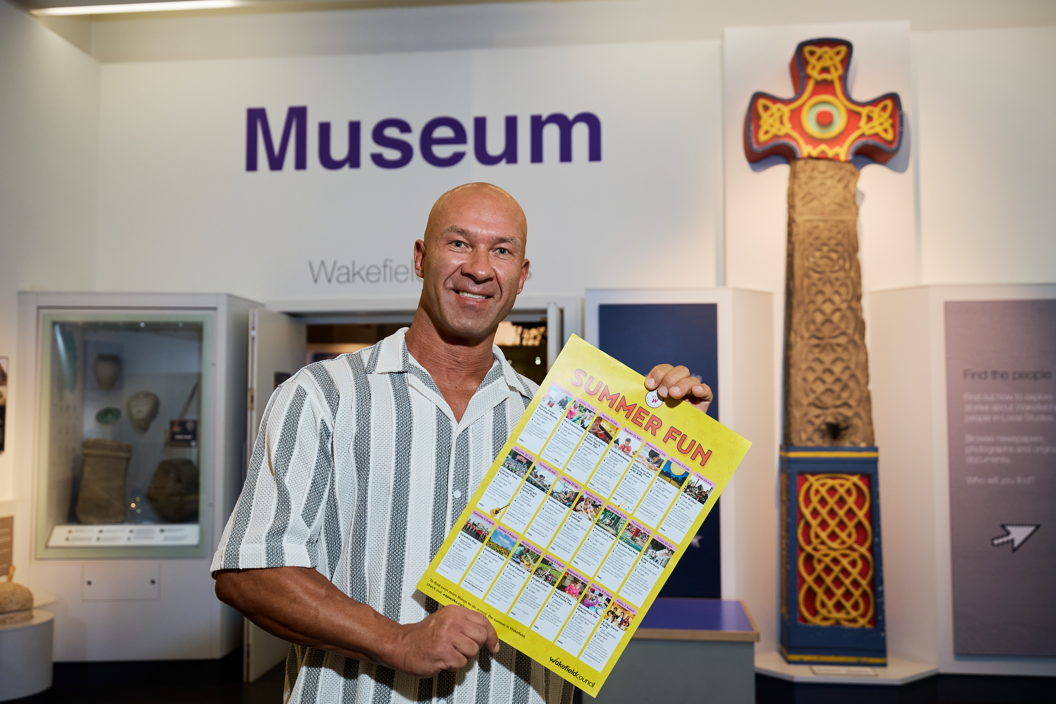 Smiling man holds summer events poster in Wakefield Museum