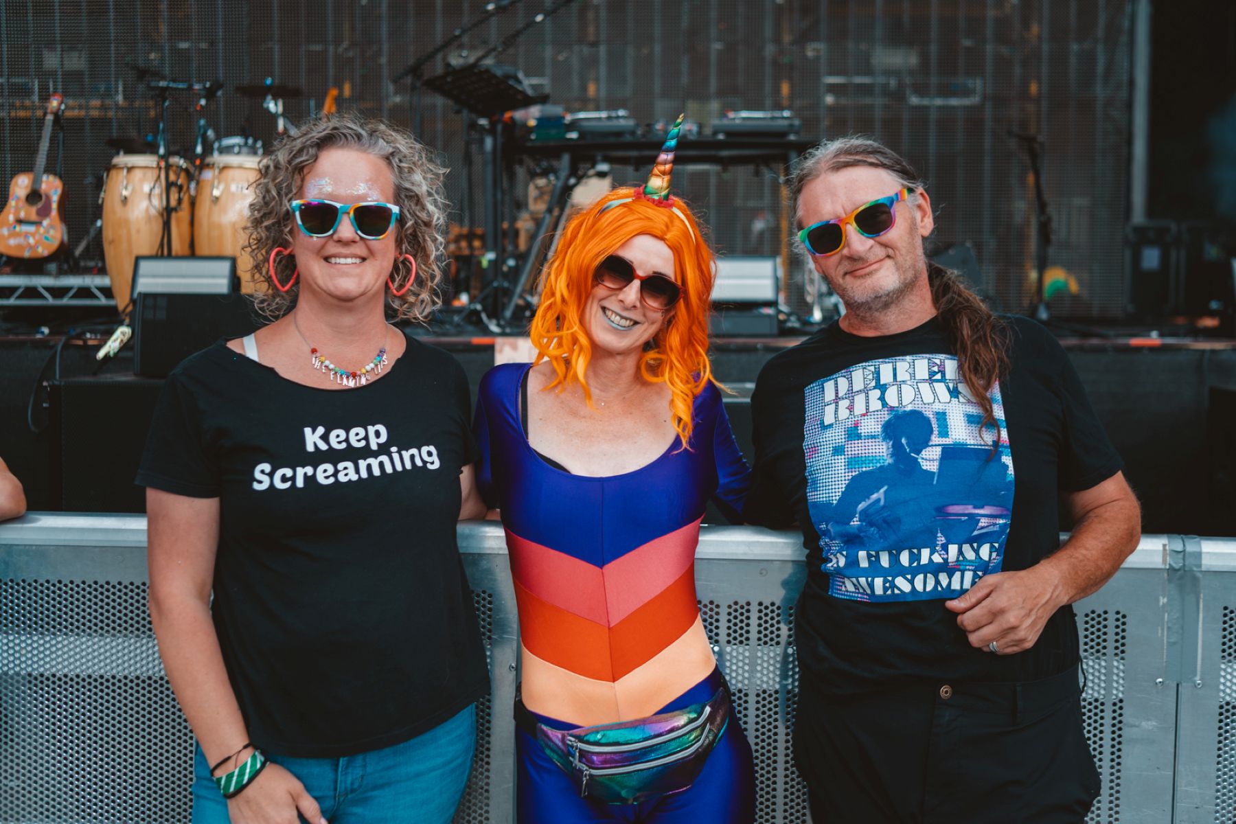 Three people in colourful attire and sunglasses at an outdoor music festival