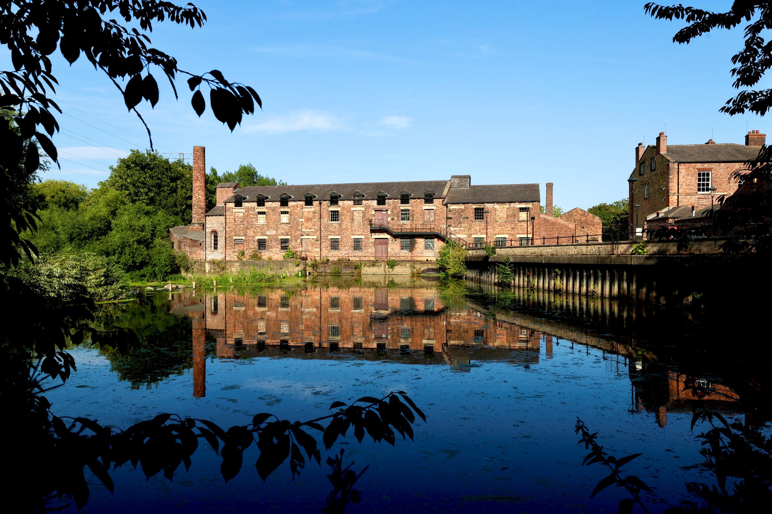 Historic red-brick mill with chimney reflecting on calm river