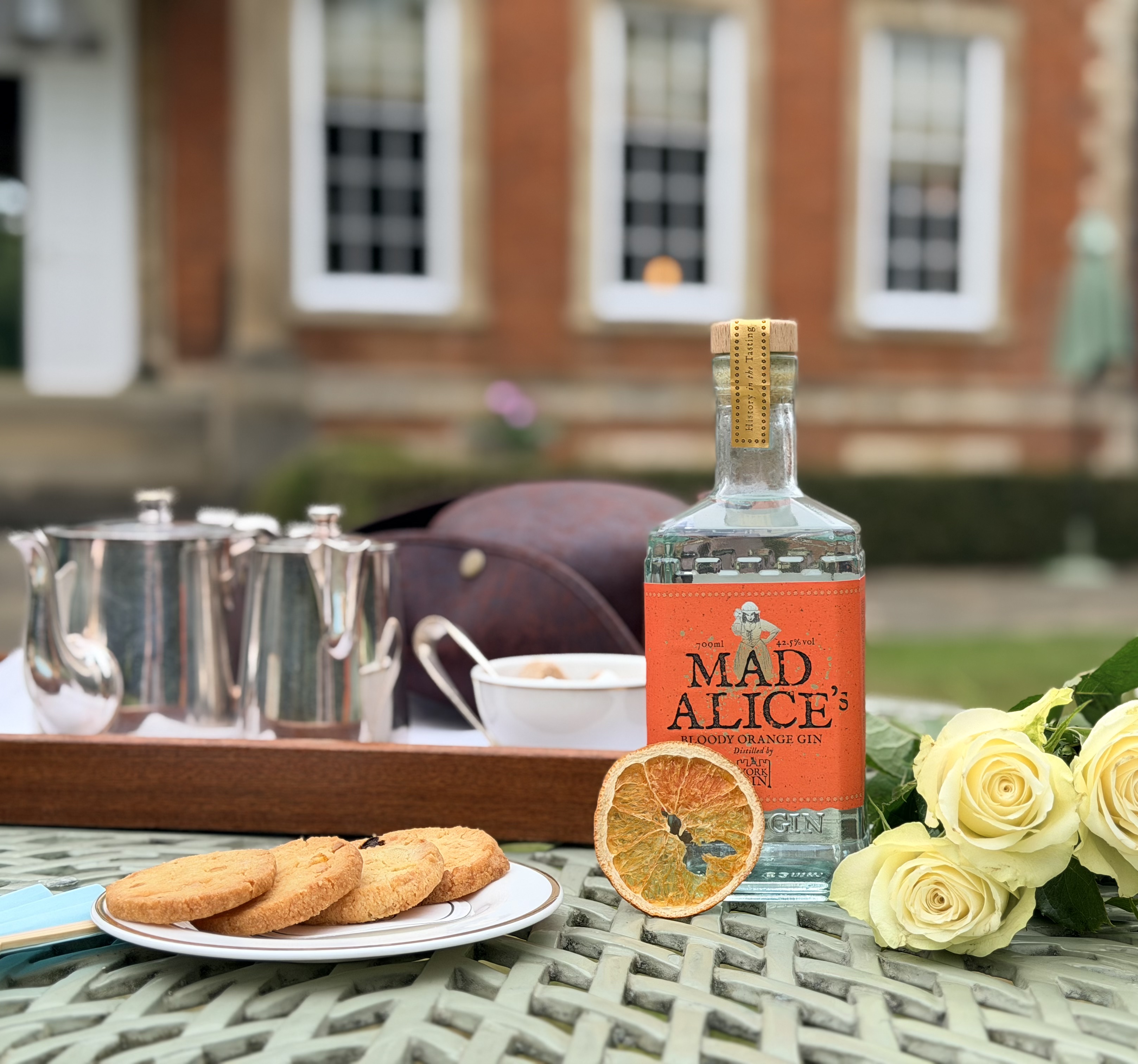 Bottled gin on table with cookies, roses, and tea set outdoors