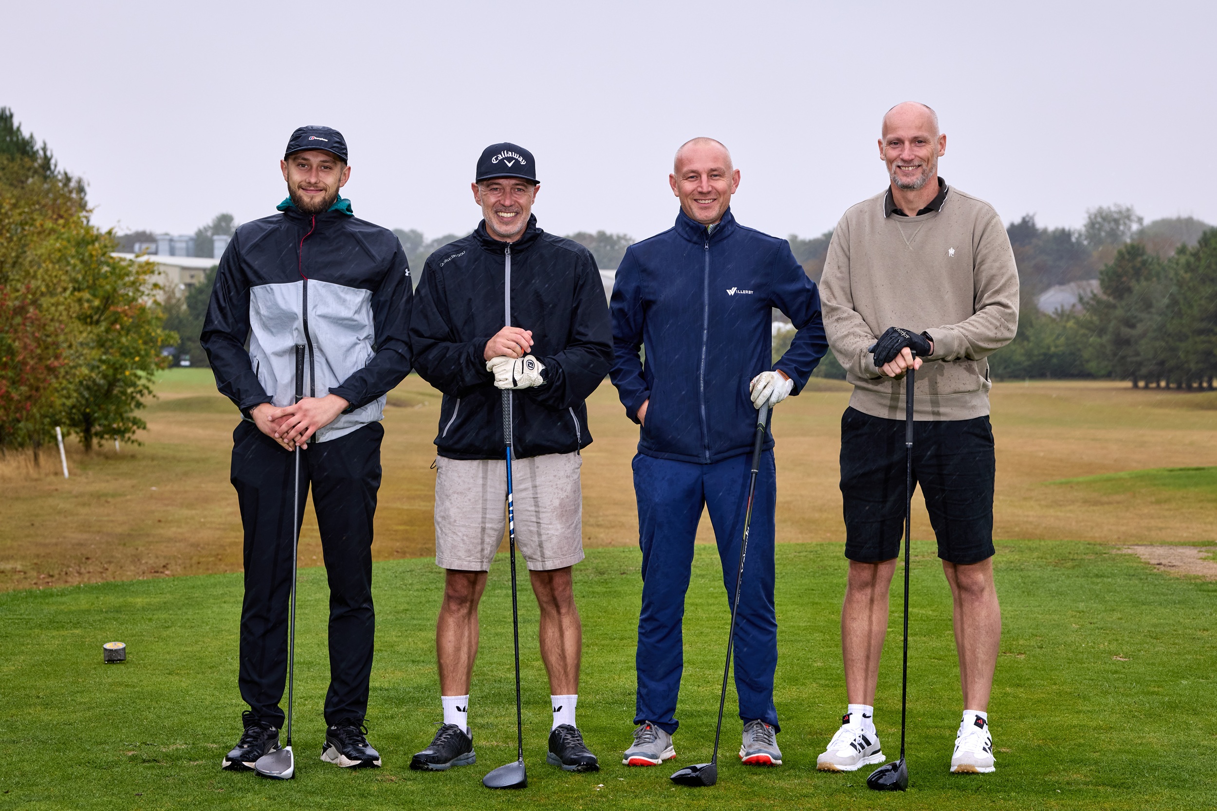 Four smiling golfers on a lush green course with trees in the background