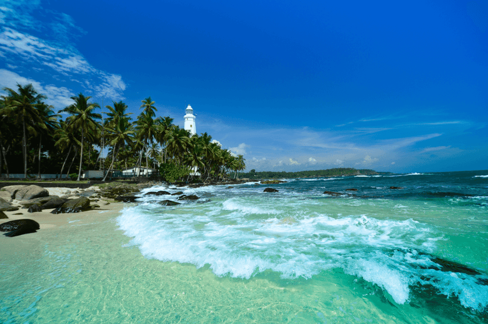 Lighthouse by palm-lined beach with clear blue sky