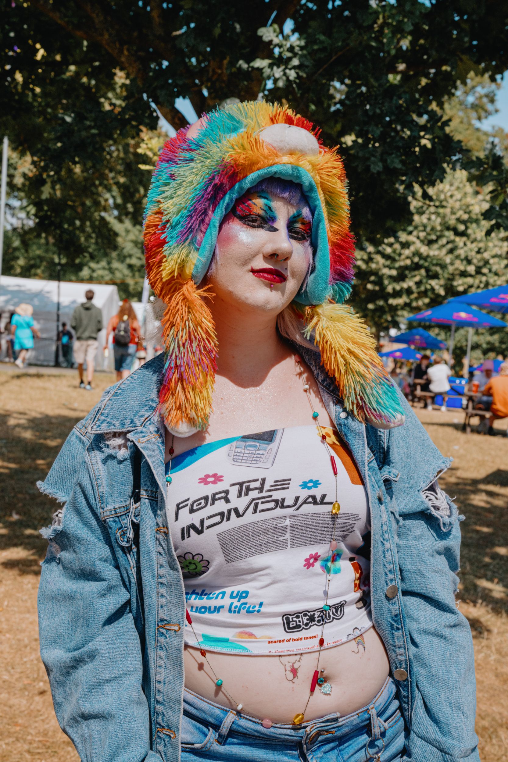 Person wearing colourful hat and denim jacket at outdoor festival
