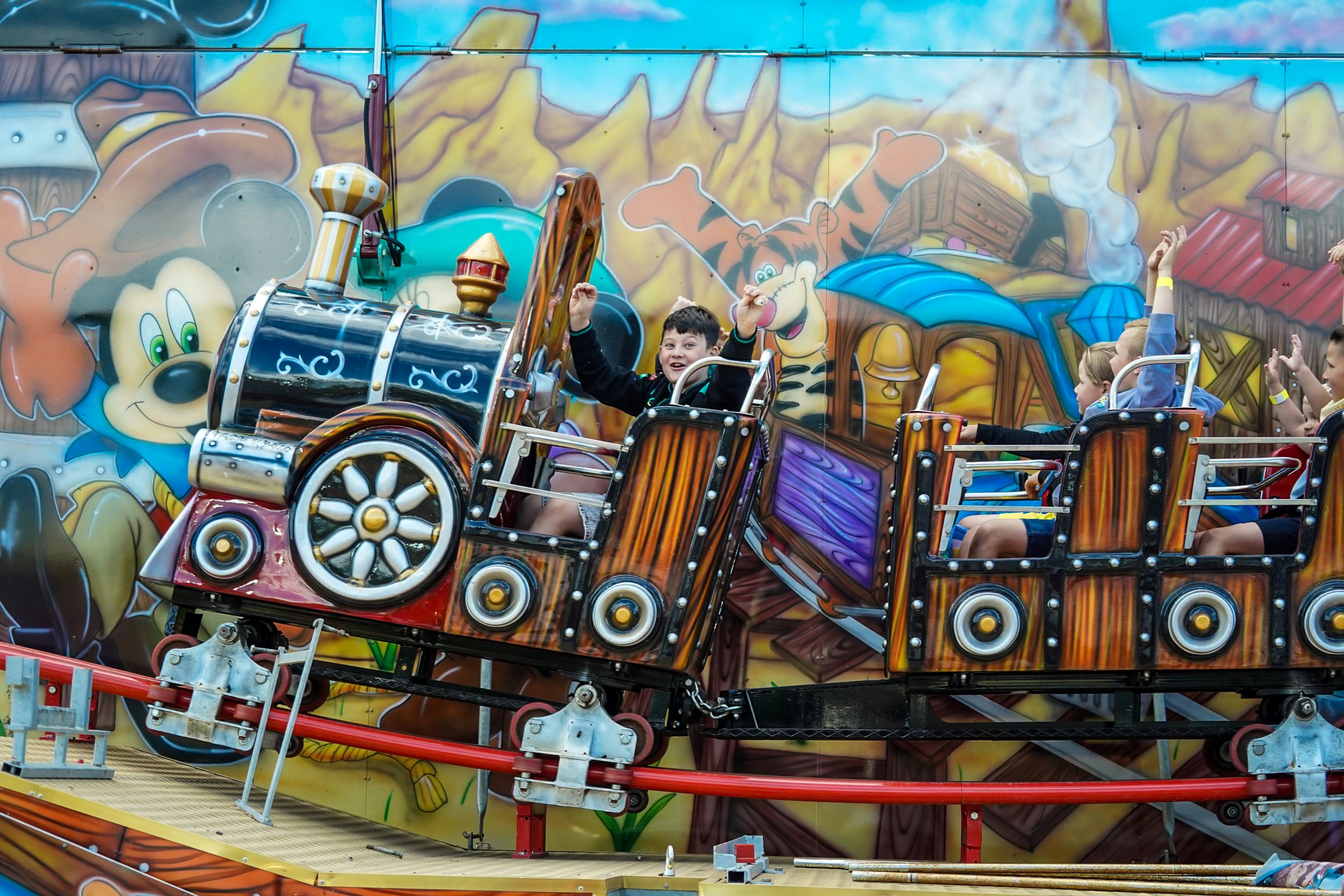Children riding a colorful train roller coaster with mural