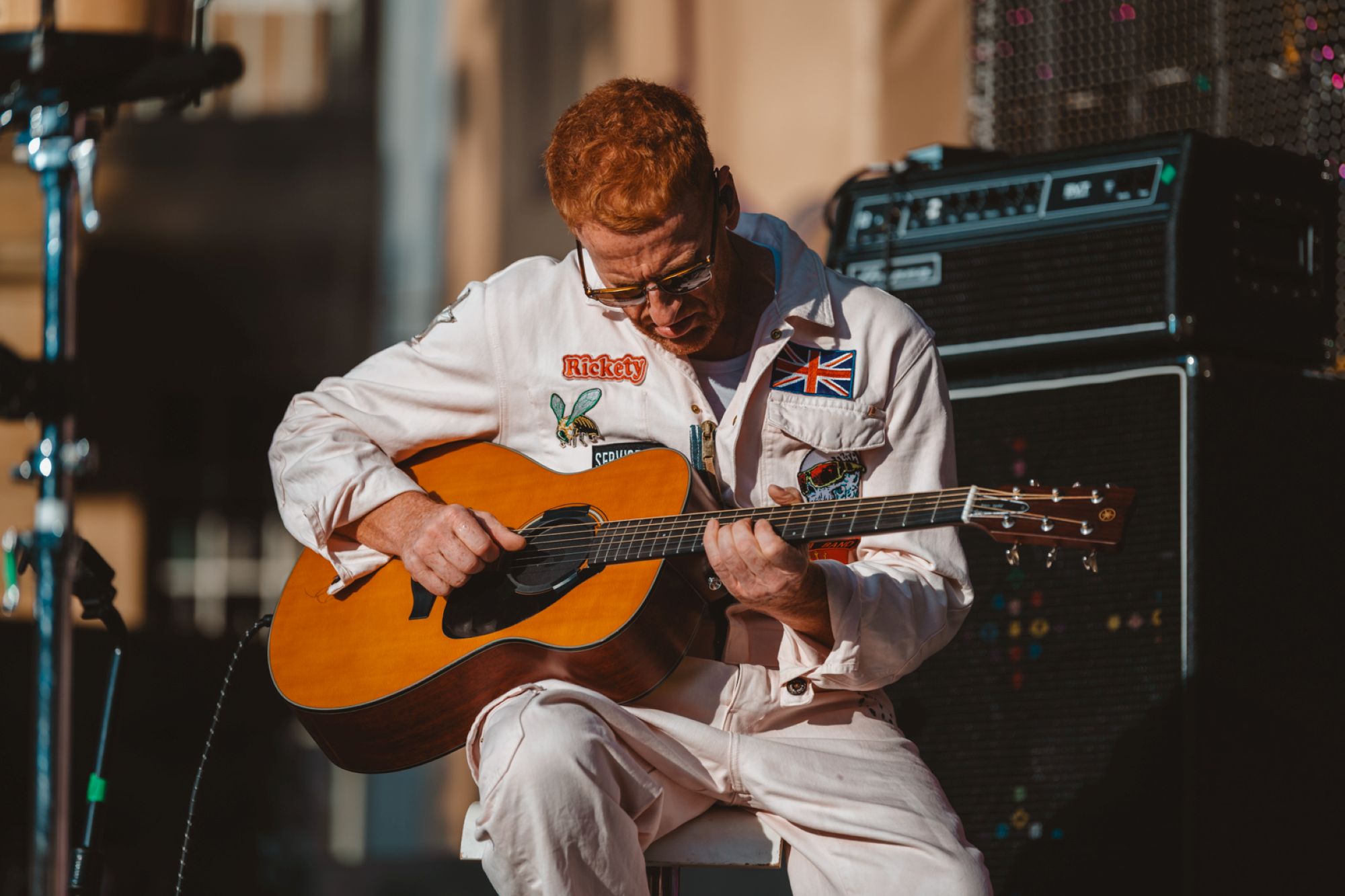 Musician in white jumpsuit playing acoustic guitar on stage