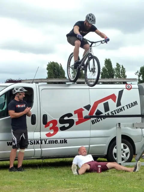 Cyclist performing stunt on van roof as man lies below