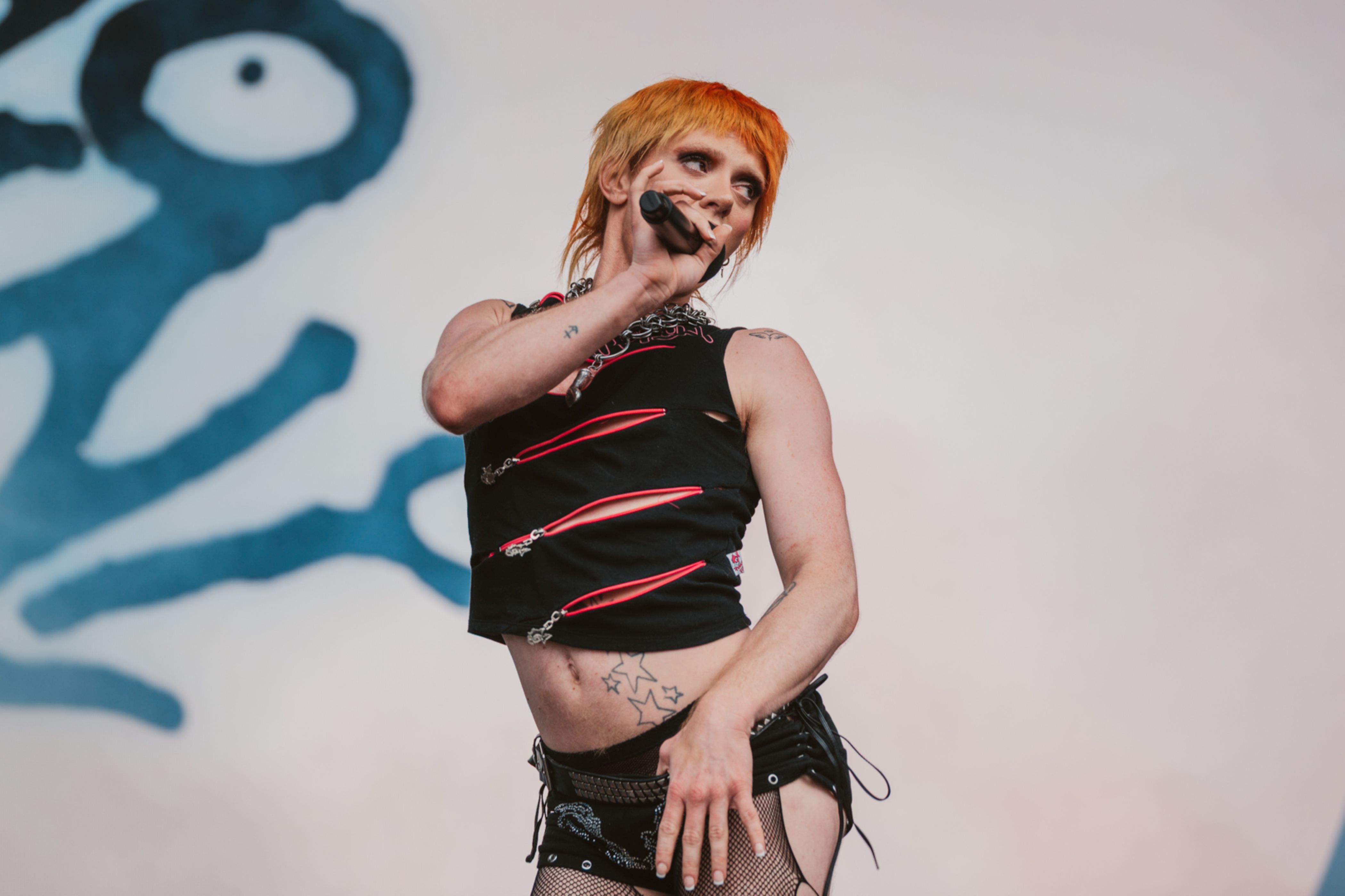 Performer with orange hair and black outfit singing on stage