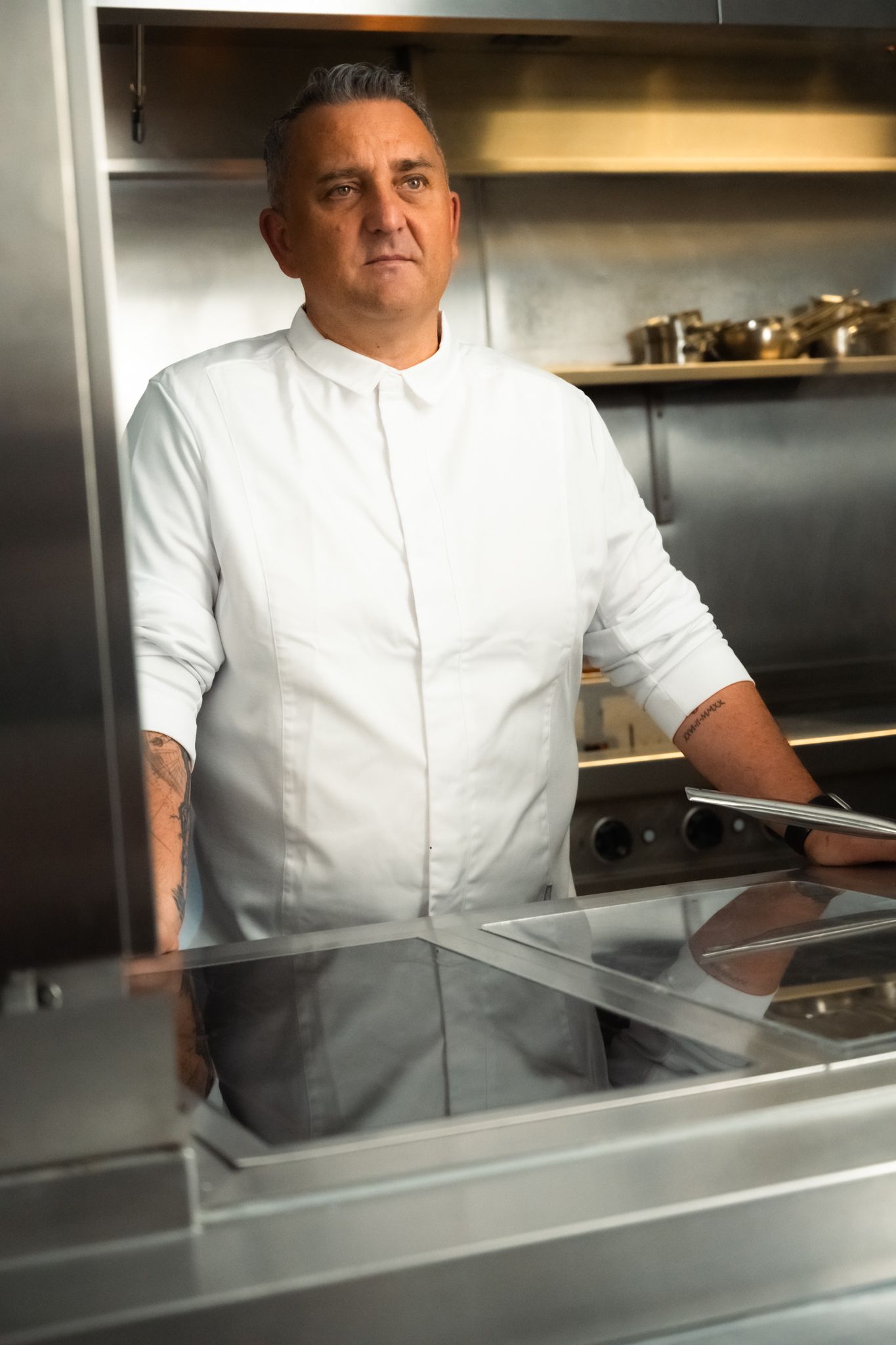 Chef in white uniform stands in stainless steel kitchen
